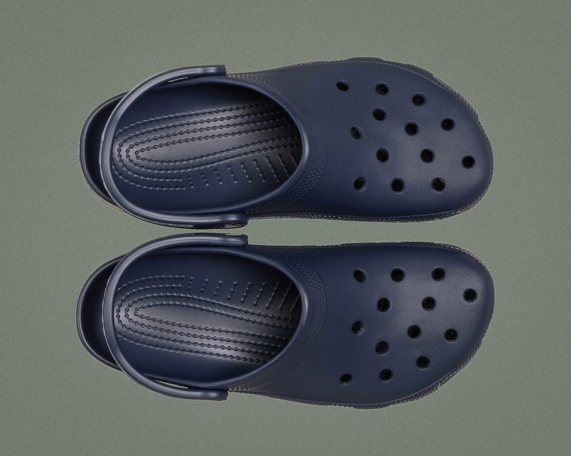 Pair of navy blue slip-on clogs with ventilation holes and adjustable heel straps on a gray surface.