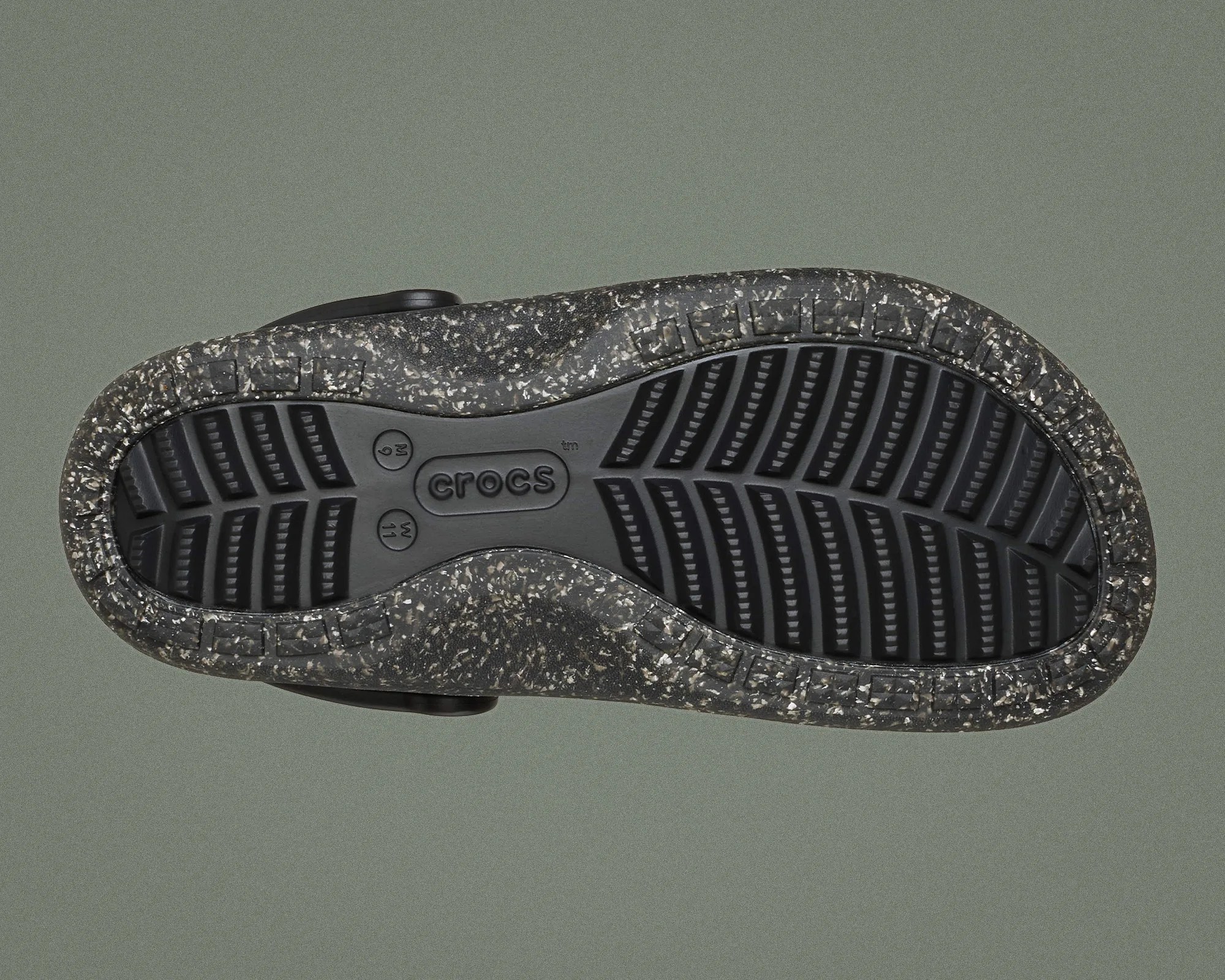Black and speckled gray Crocs sole with textured tread on a gray background.