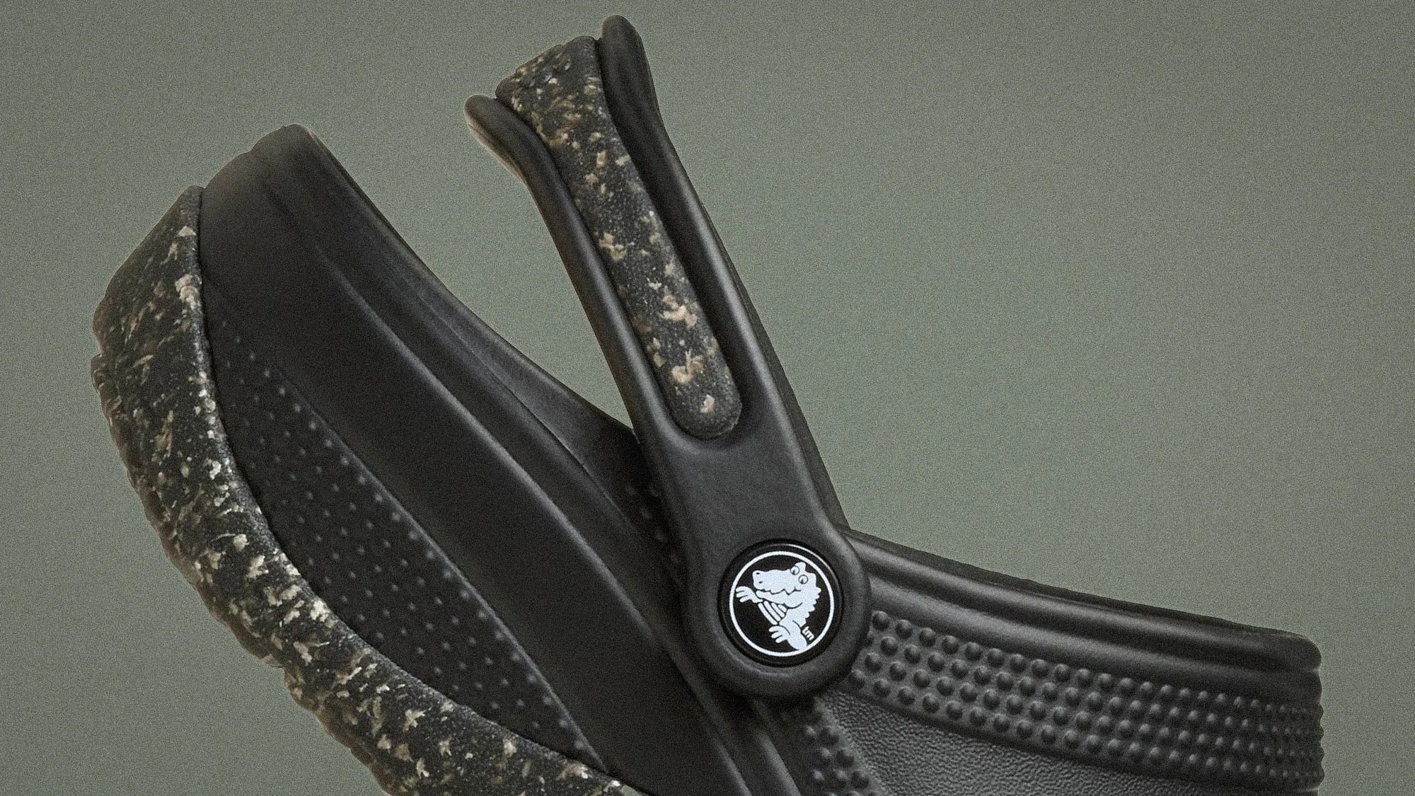 Close-up of black Crocs shoe with speckled sole and textured strap featuring a circular logo with a crocodile.
