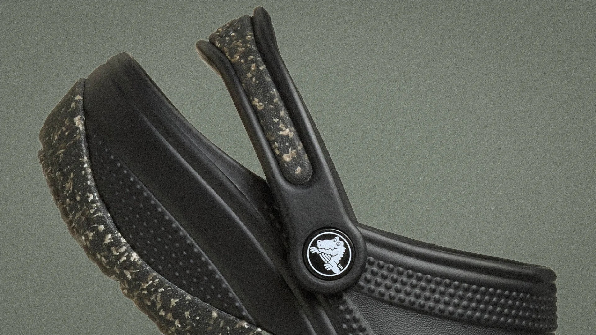 Close-up of black Crocs shoe with speckled sole and textured strap featuring a circular logo with a crocodile.