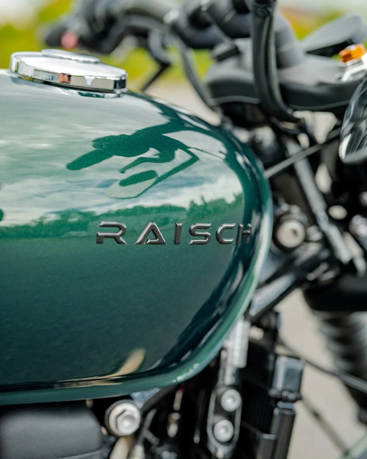 Glossy dark green motorcycle fuel tank with chrome cap and "RAISCH" emblem.