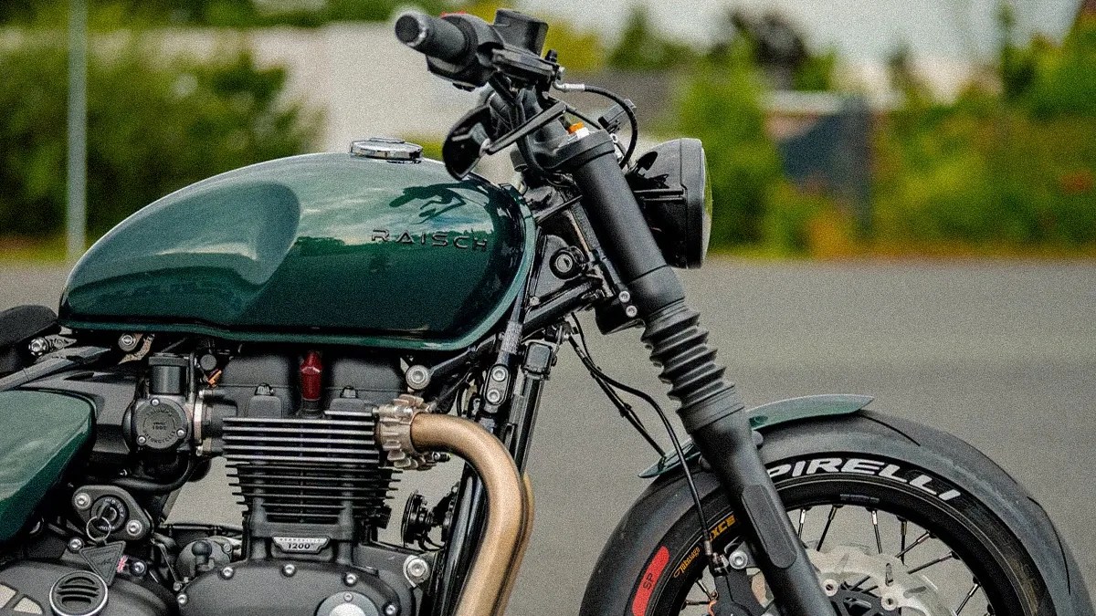 Close-up of a dark green Raisch motorcycle fuel tank and front wheel with Pirelli tire on a paved surface.