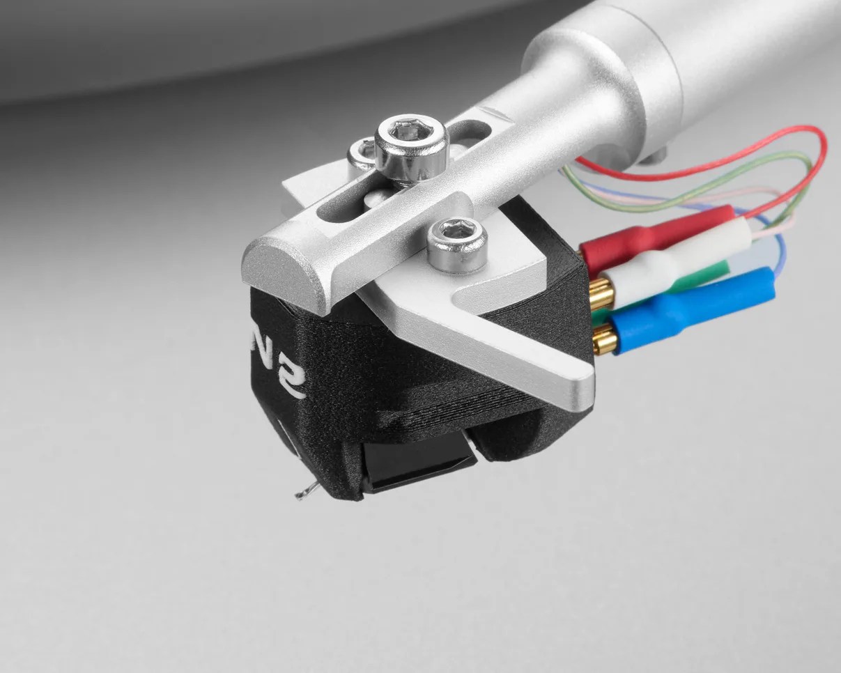 Close-up of a silver tonearm with a black cartridge and red, white, blue, and green wires attached.