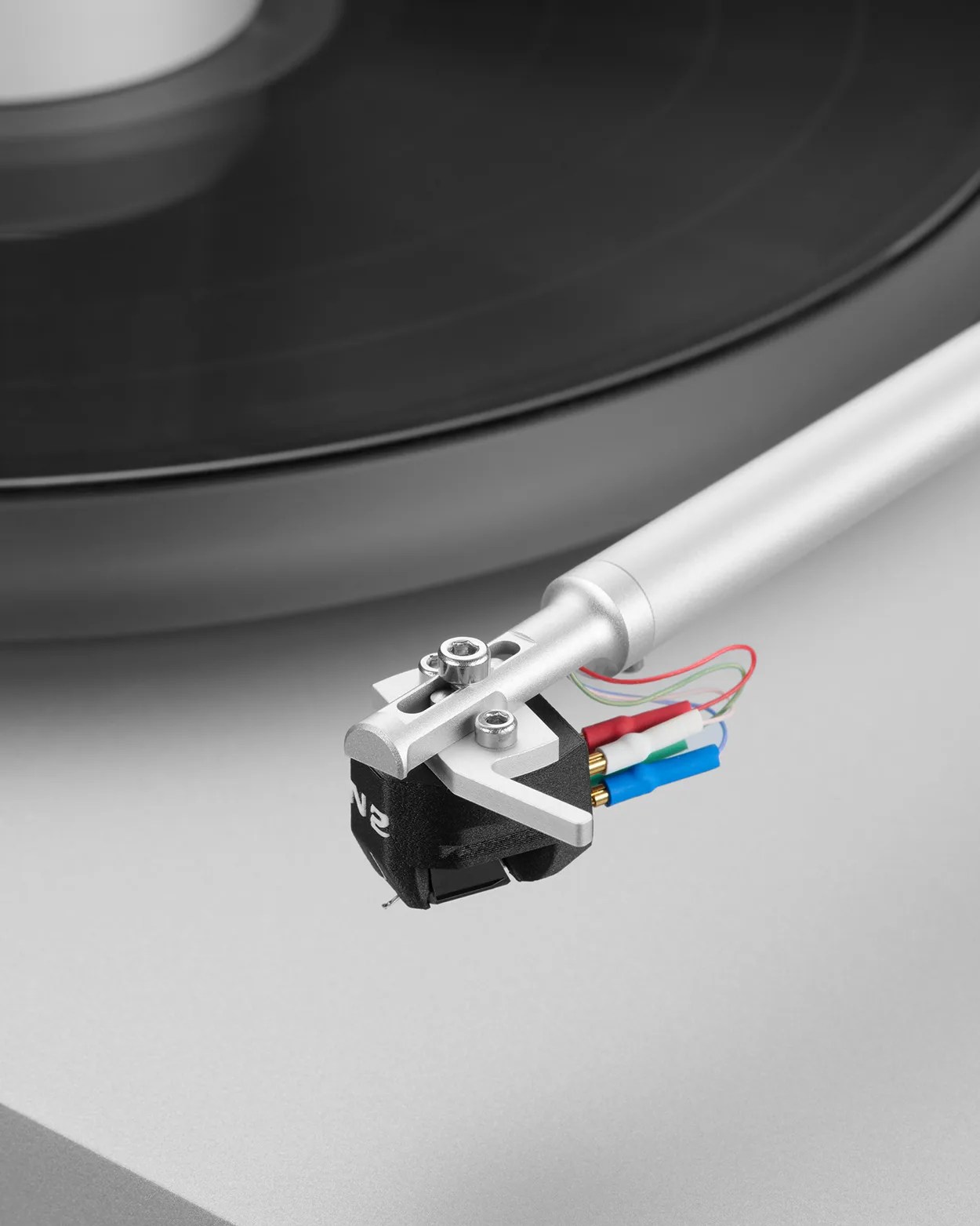 Close-up of a silver tonearm with a black cartridge and colored wires on a gray turntable.