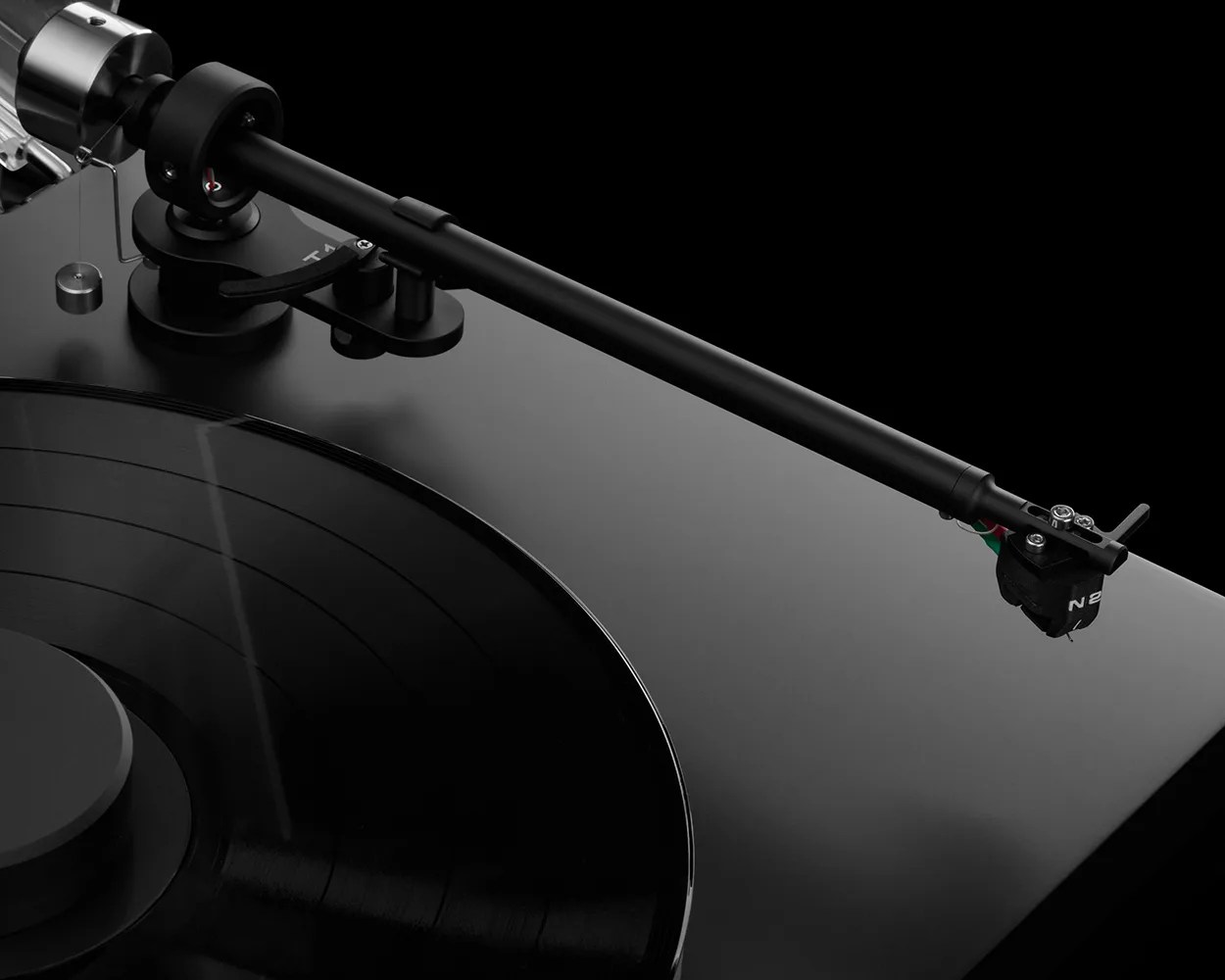 Close-up of a black turntable tonearm and cartridge over a spinning vinyl record on a glossy black base.