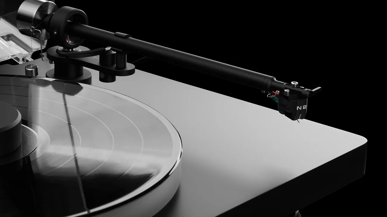 Close-up of a black and silver turntable tonearm positioned over a spinning vinyl record on a gray base.