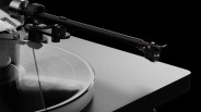 Close-up of a black and silver turntable tonearm positioned over a spinning vinyl record on a gray base.