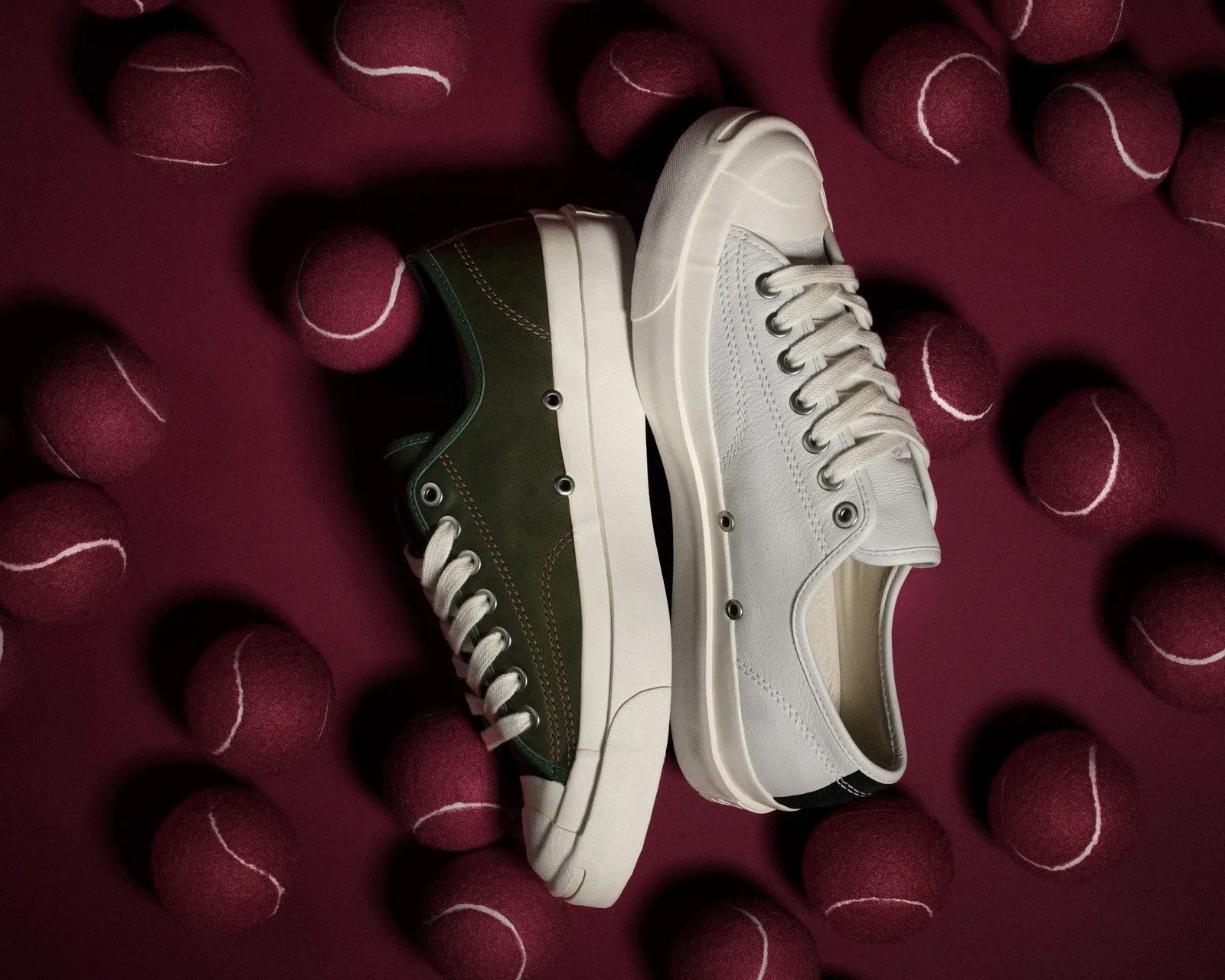 Pair of low-top sneakers, one olive green and one white, surrounded by maroon tennis balls on a maroon surface.