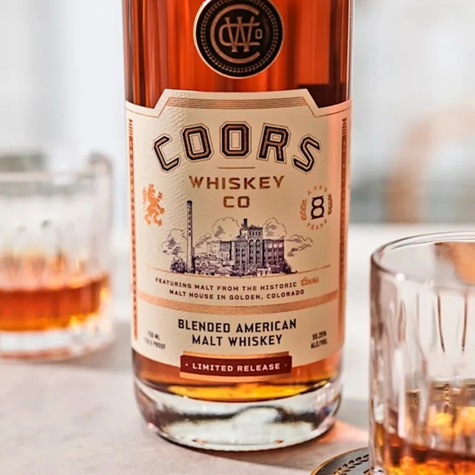 Close-up of a Coors Whiskey Co. blended American malt whiskey bottle with amber liquid and a glass partially filled with whiskey.