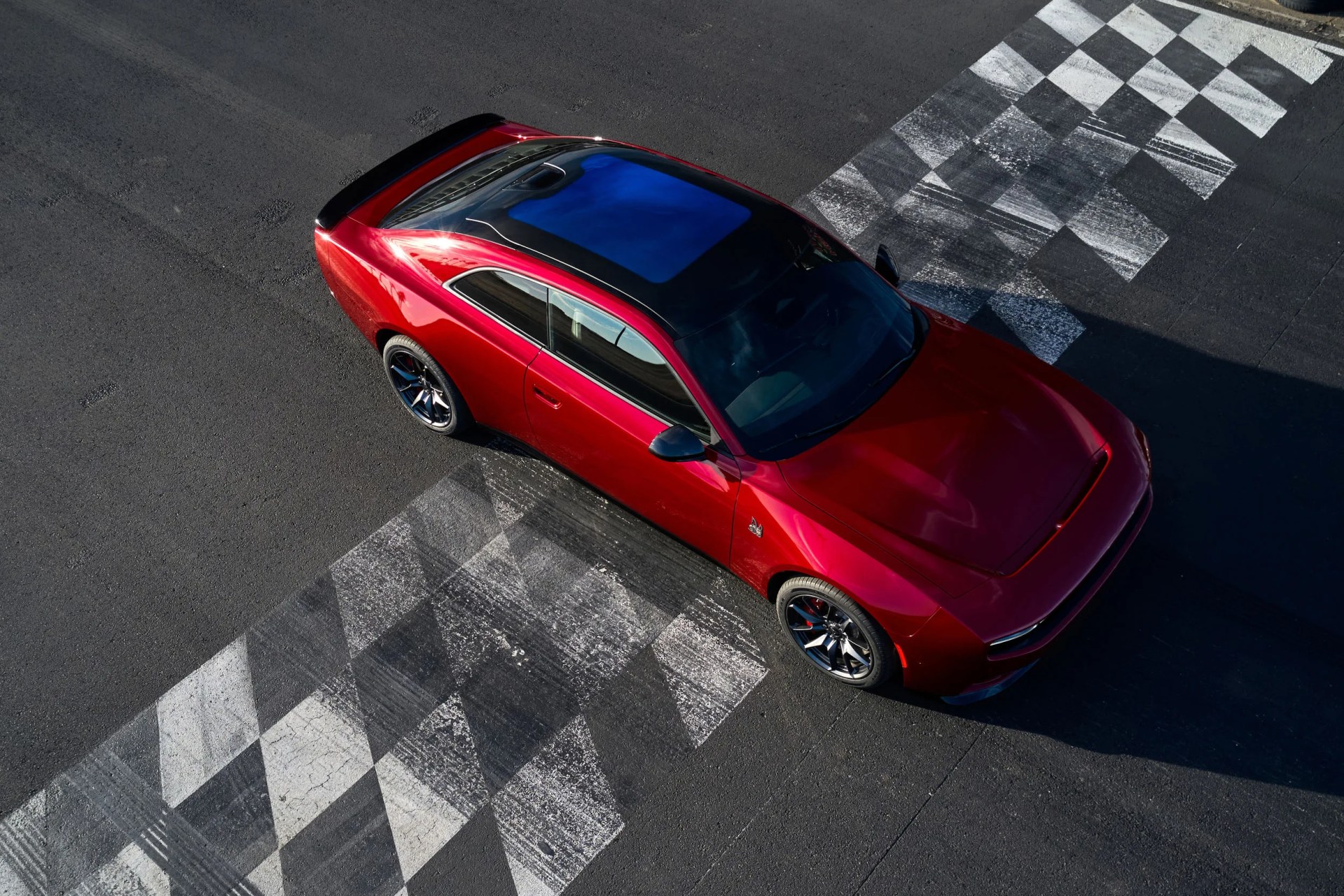 Red sports car with black roof and tinted windows on a checkered race track finish line.