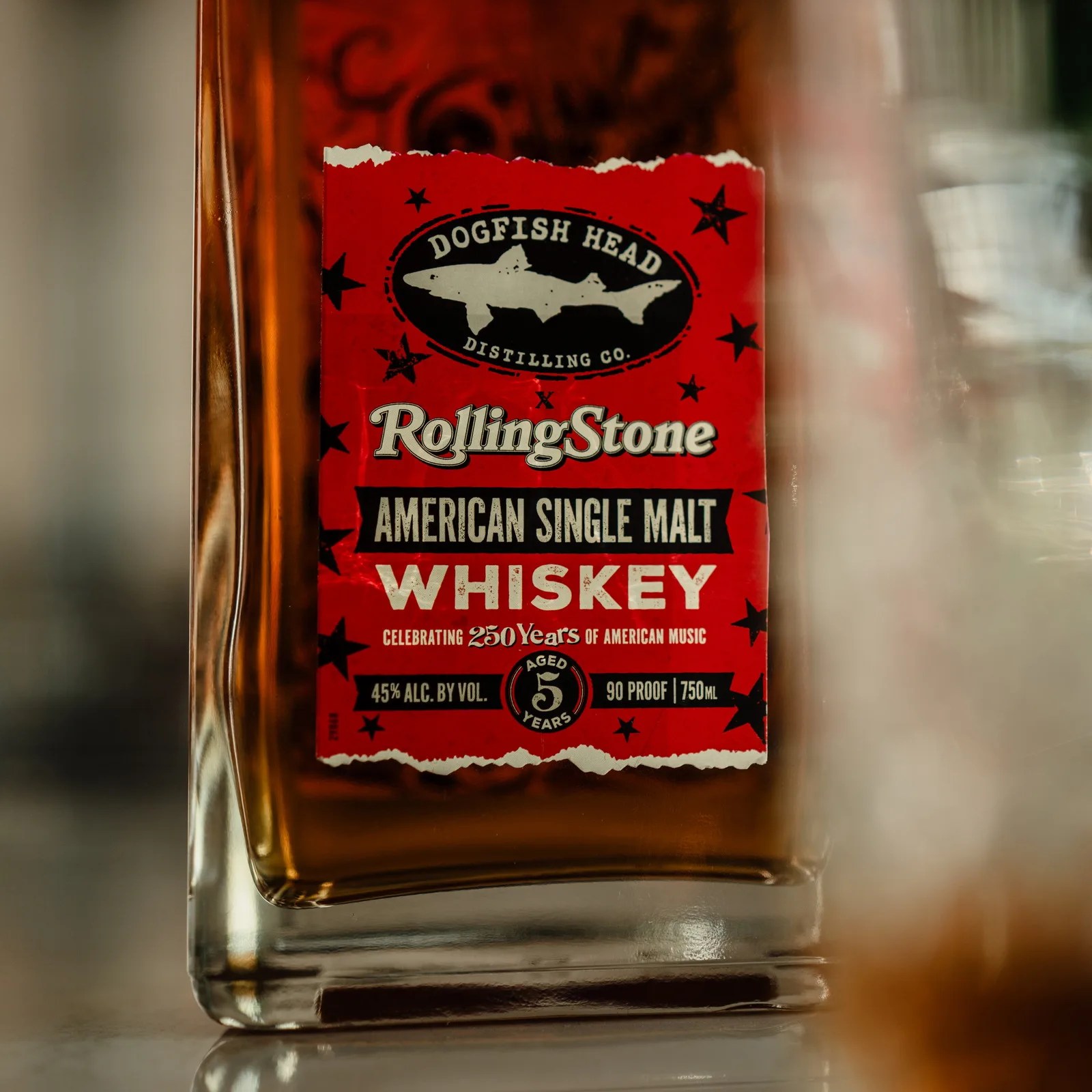 Close-up of a whiskey bottle label reading "Dogfish Head Distilling Co. Rolling Stone American Single Malt Whiskey, aged 5 years, 45% alc. by vol., 90 proof, 750 ml.