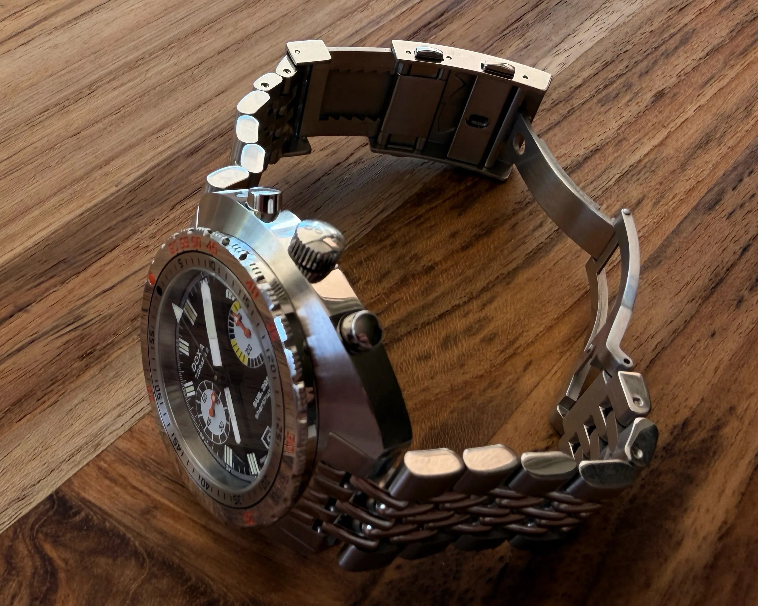 Stainless steel wristwatch with black dial, chronograph subdials, and metal link bracelet on a wooden surface.