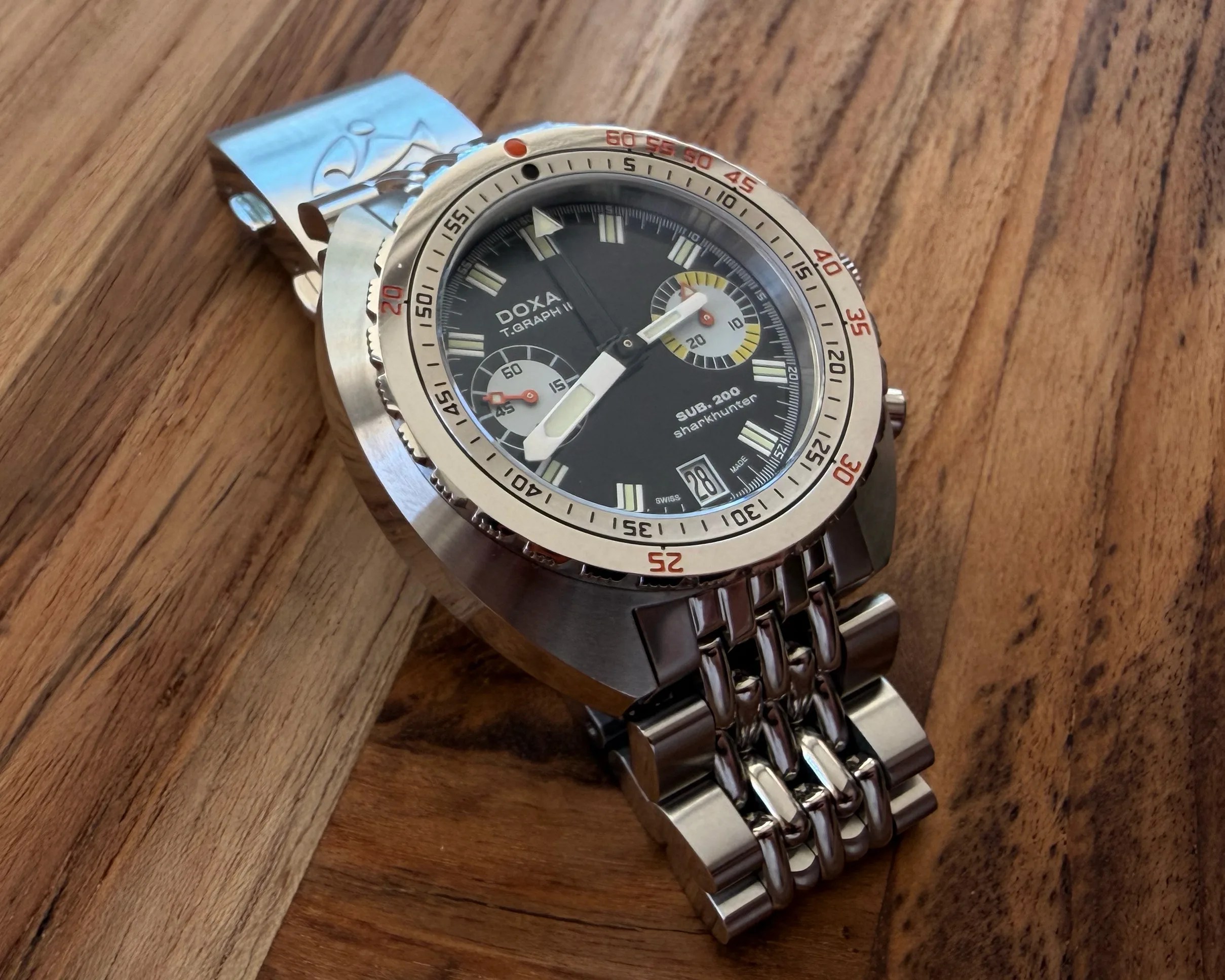 Stainless steel Doxa T.Graph II SUB 200 Sharkhunter wristwatch with black dial and metal bracelet on wooden surface.