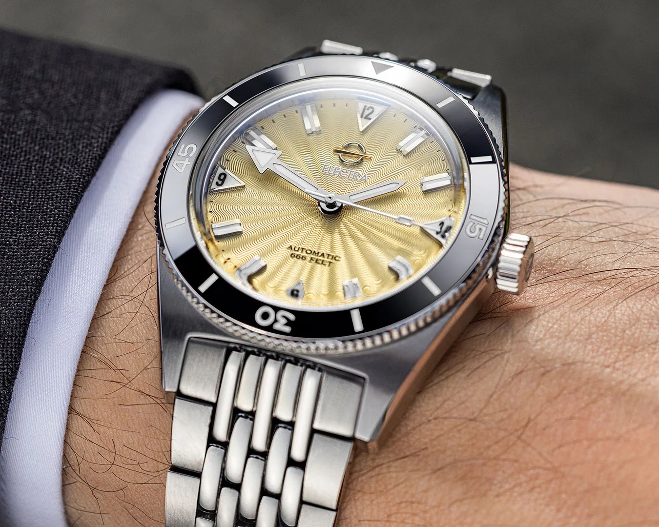 Silver metal wristwatch with a textured gold dial, black bezel, and stainless steel bracelet worn on a wrist.