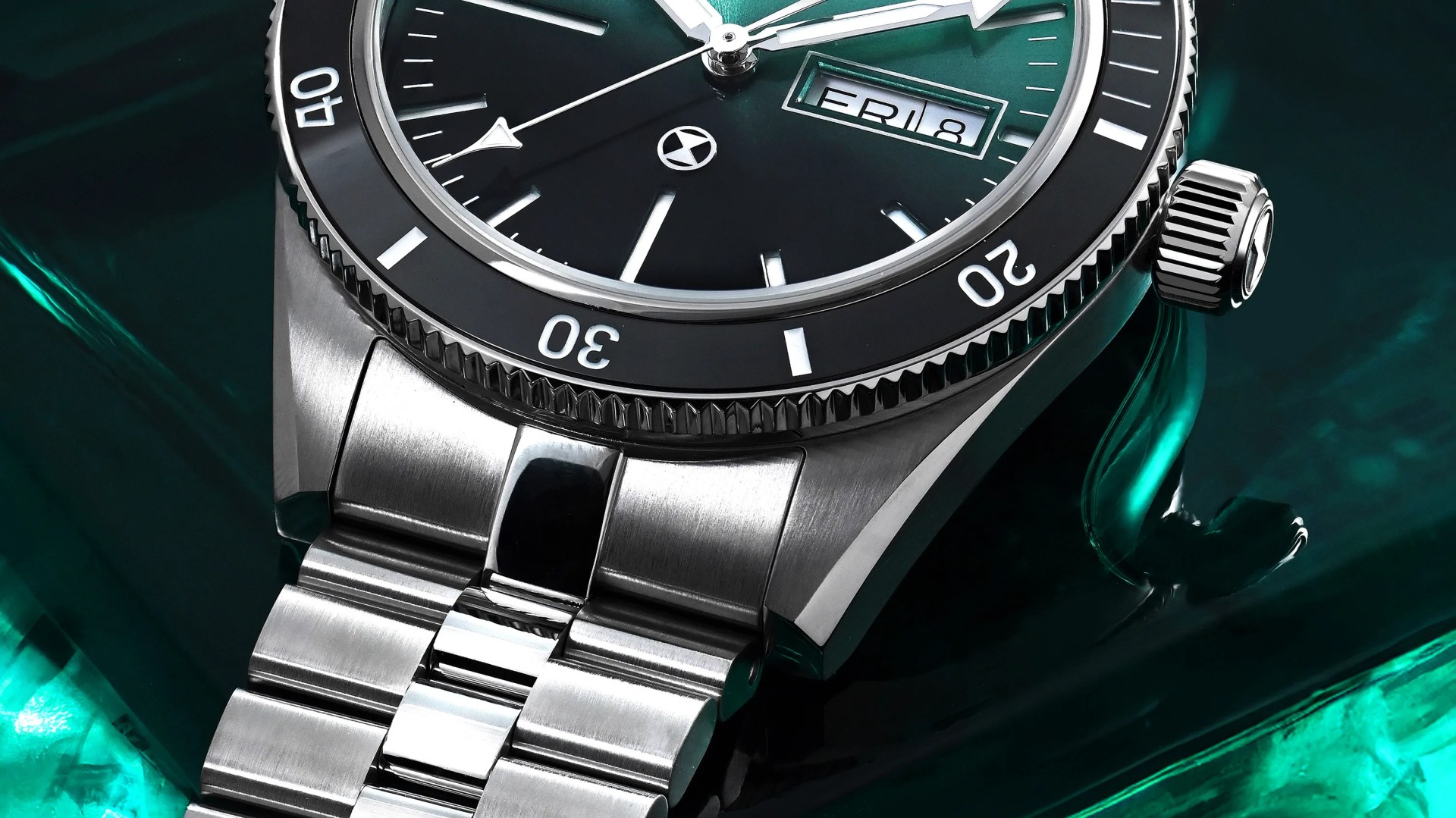 Close-up of a stainless steel wristwatch with a black bezel, black dial, day-date display, and silver bracelet on a green reflective surface.
