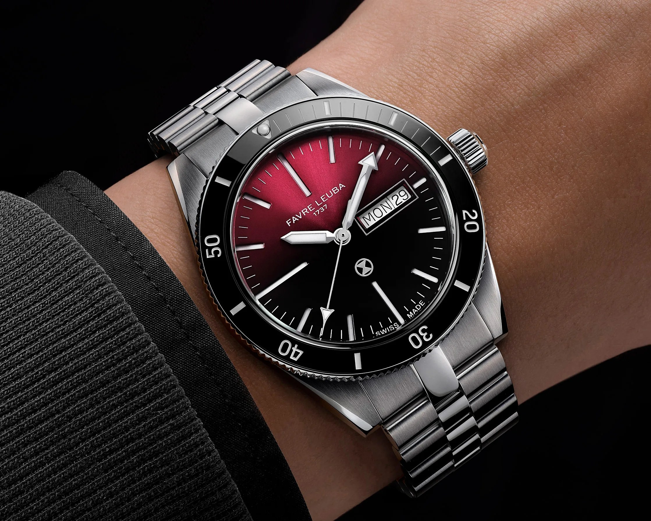 Stainless steel wristwatch with black and red gradient dial, day-date display, and rotating bezel on a wrist.
