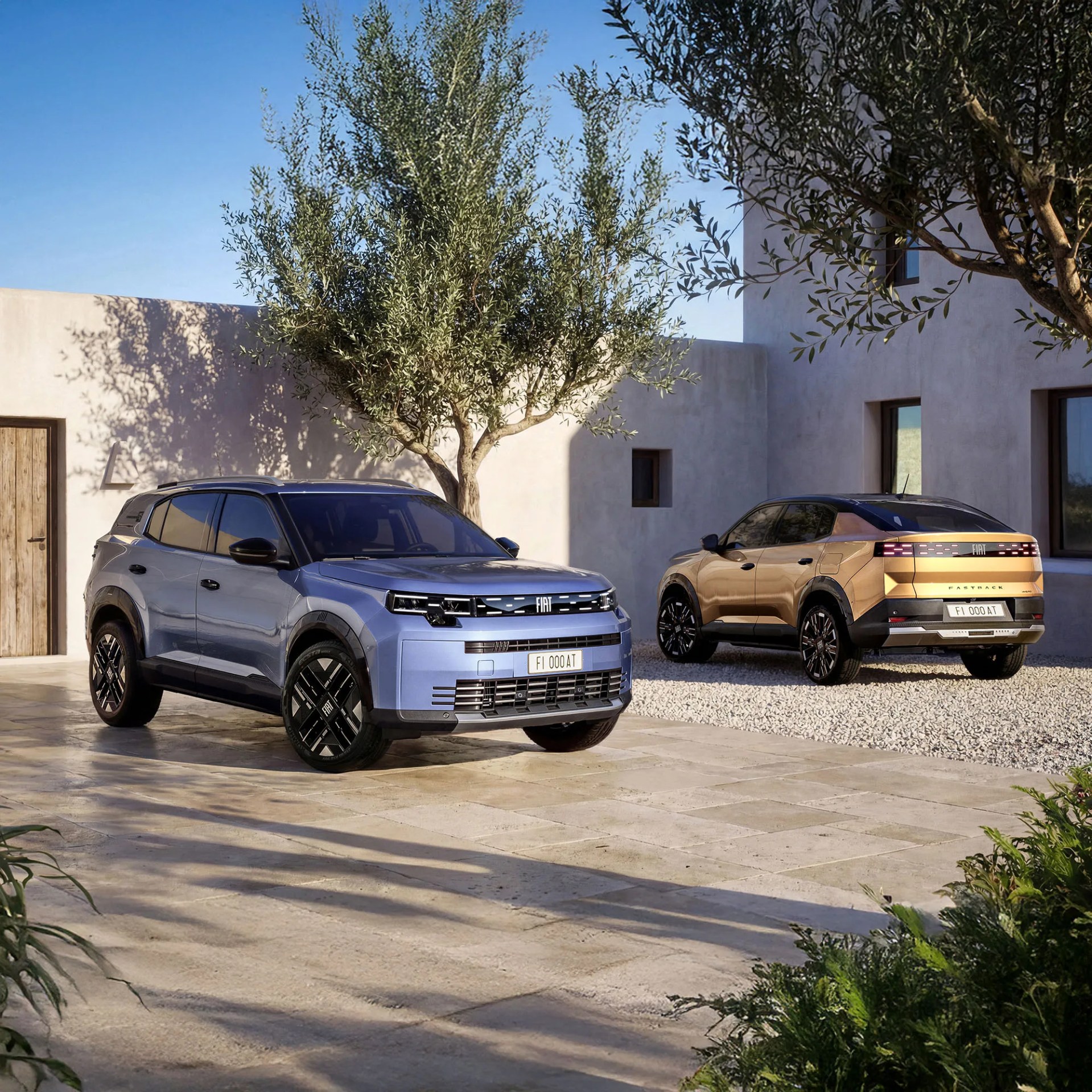 Two modern Fiat SUVs, one blue and one gold, parked outside a beige stucco building with olive trees.