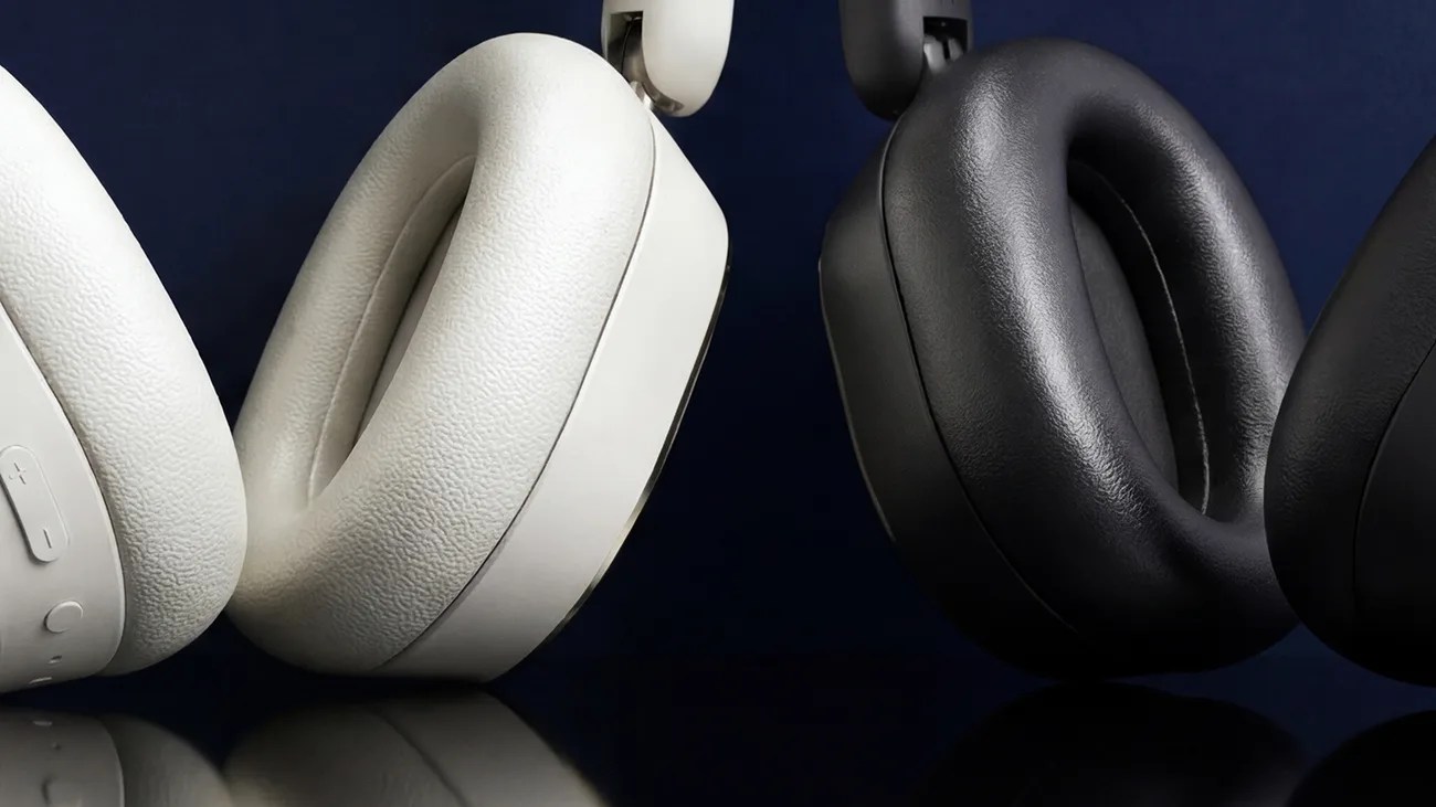 Close-up of white and black over-ear headphone ear cushions against a dark background.