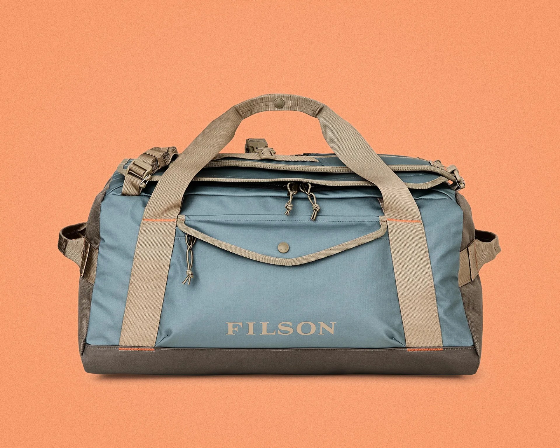 Blue and gray Filson duffel bag with beige straps and zipper pulls on an orange background.