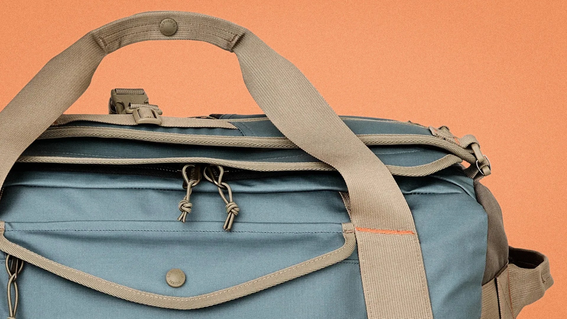 Blue fabric bag with beige straps and zipper pulls against an orange background.