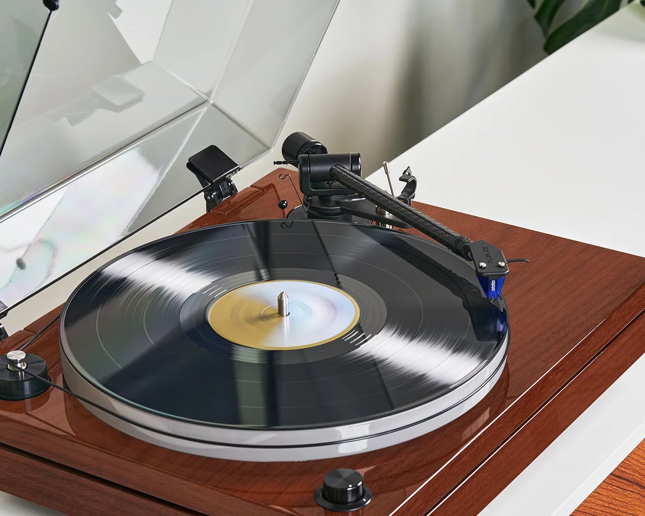 Turntable with a spinning black vinyl record on a wooden base with a clear dust cover.