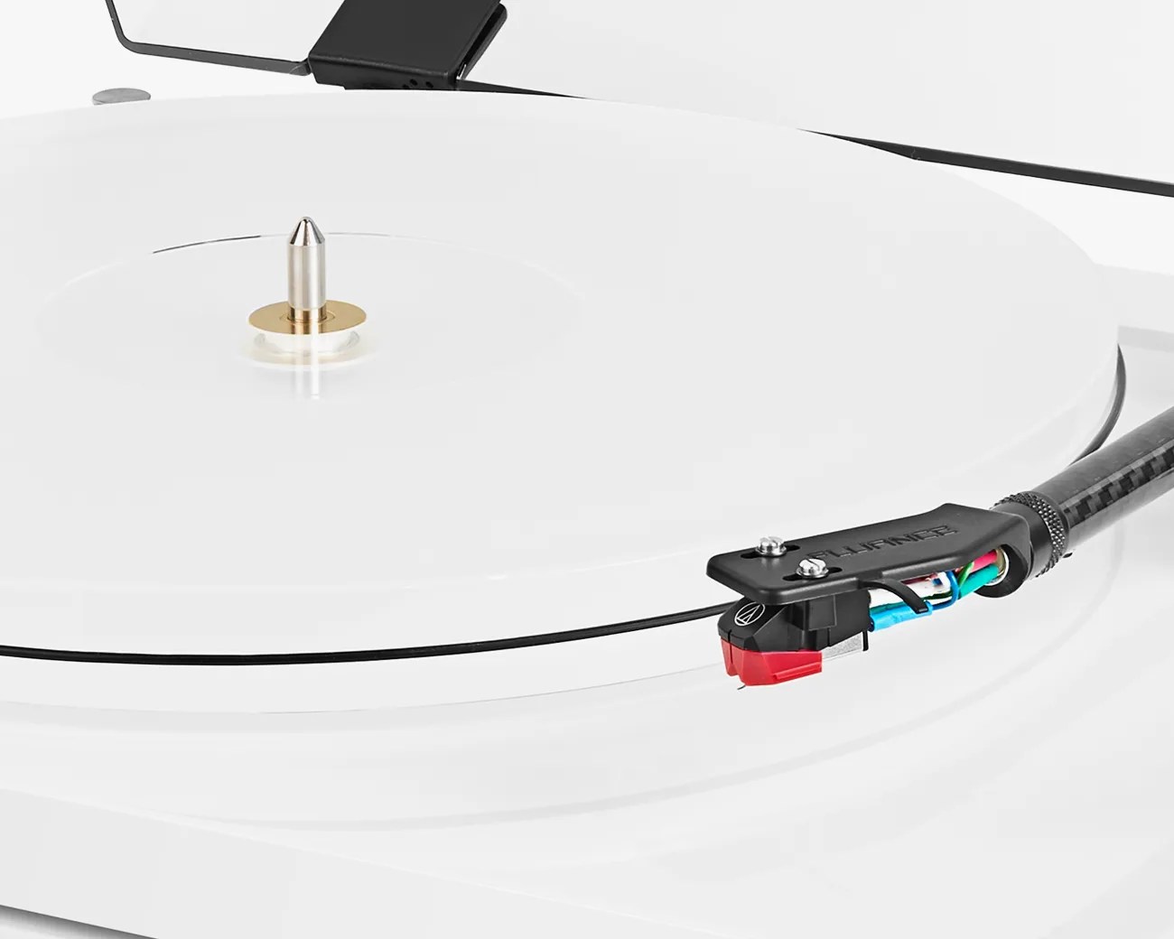 Close-up of a white turntable with a black tonearm and red cartridge on a white vinyl record.