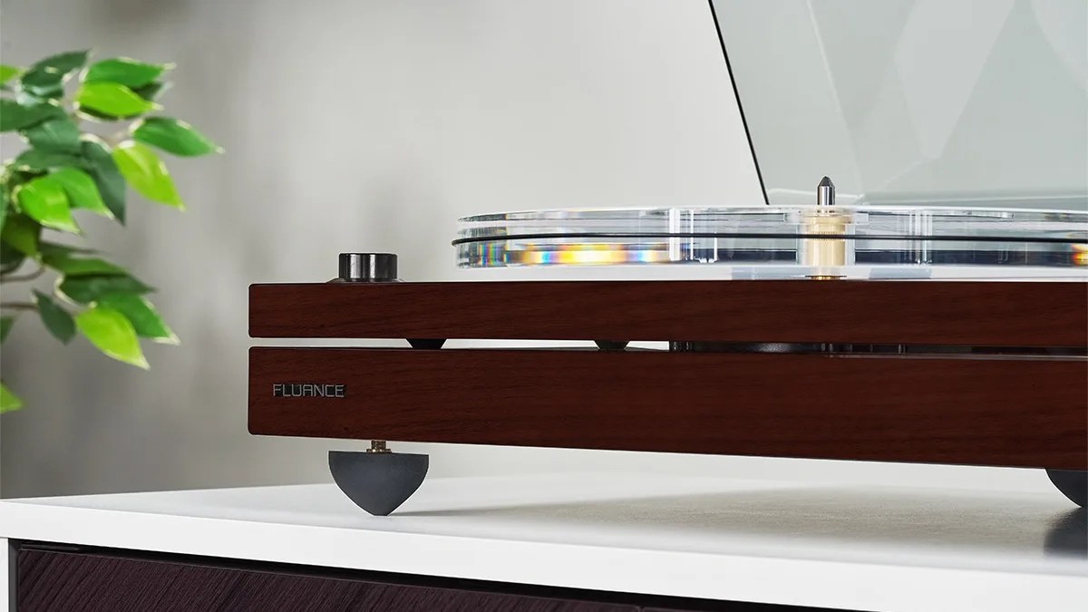 Wooden Fluance turntable with clear acrylic platter on a white surface next to green plant leaves.