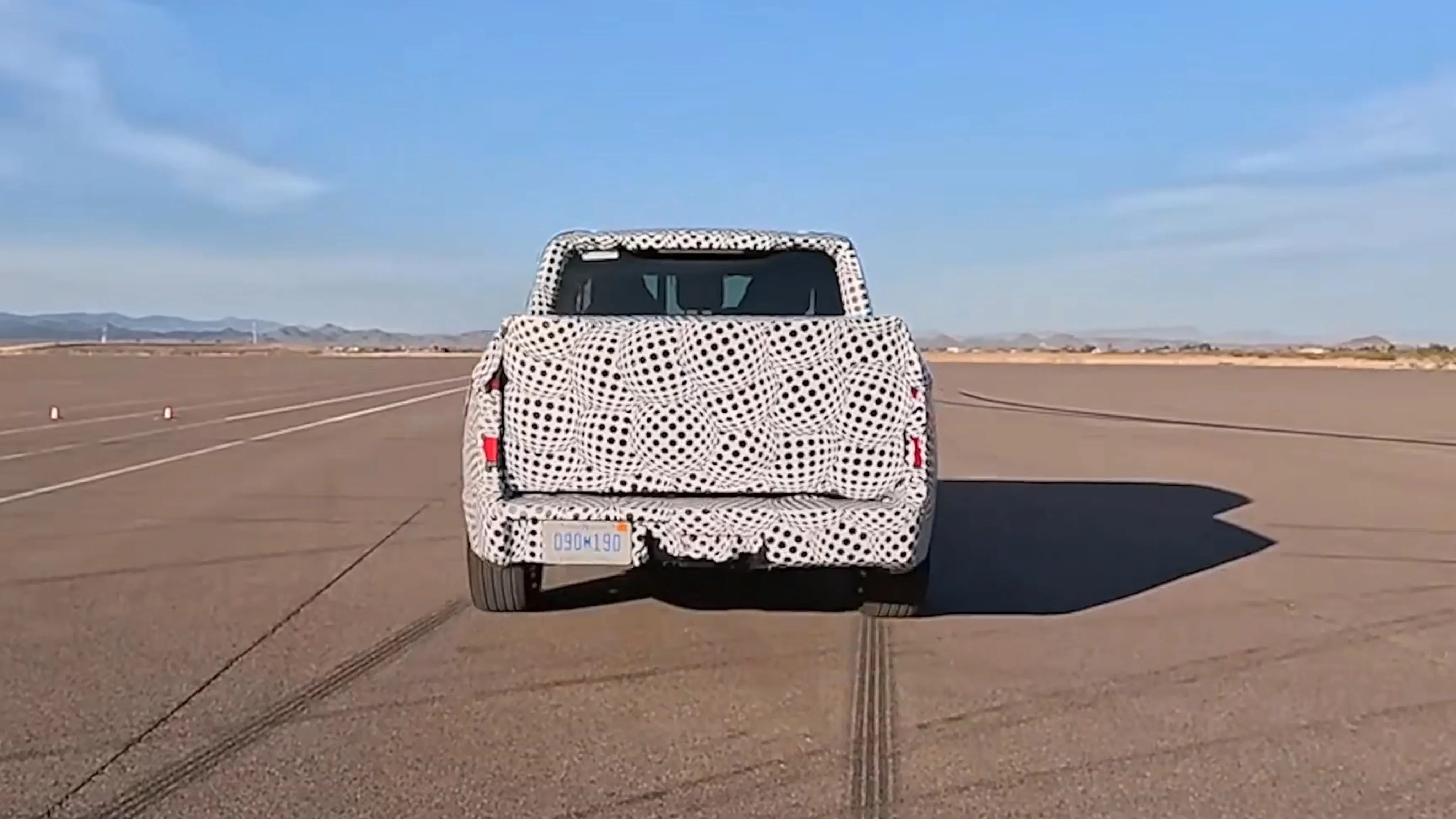 Pickup truck covered in black and white circular camouflage wrap on a wide paved area under a clear blue sky.