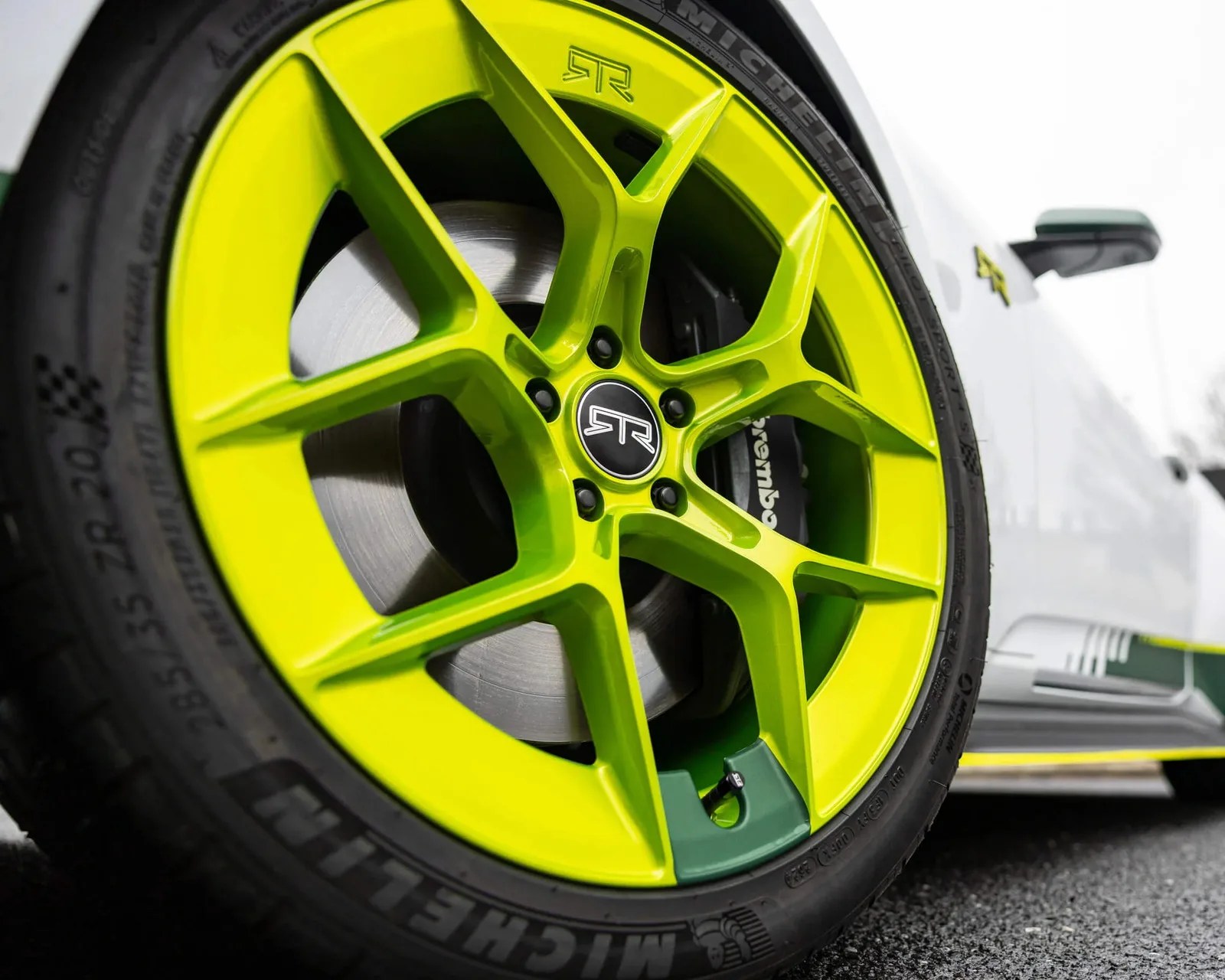 Bright lime green five-spoke alloy wheel with black center cap and Michelin tire on a white car.