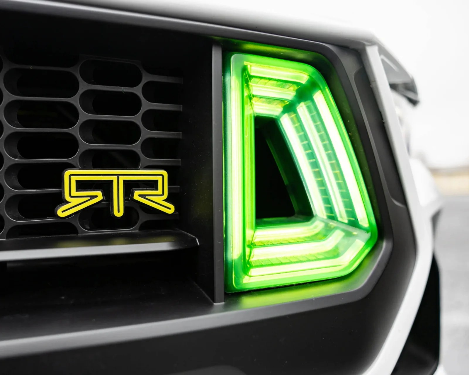 Close-up of a car front grille with a yellow RTR logo and a bright green LED headlight.