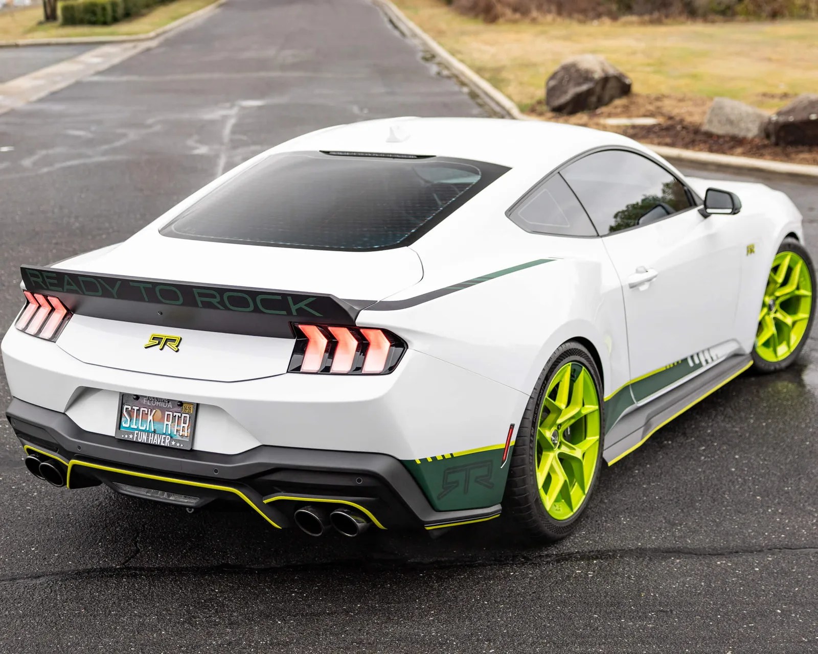 White sports car with neon green wheels, "READY TO ROCK" spoiler, and Florida license plate "SICK RTR" on wet pavement.