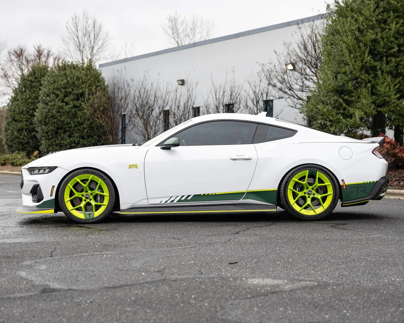 White sports coupe with neon green wheels and green and yellow side decals parked on asphalt.