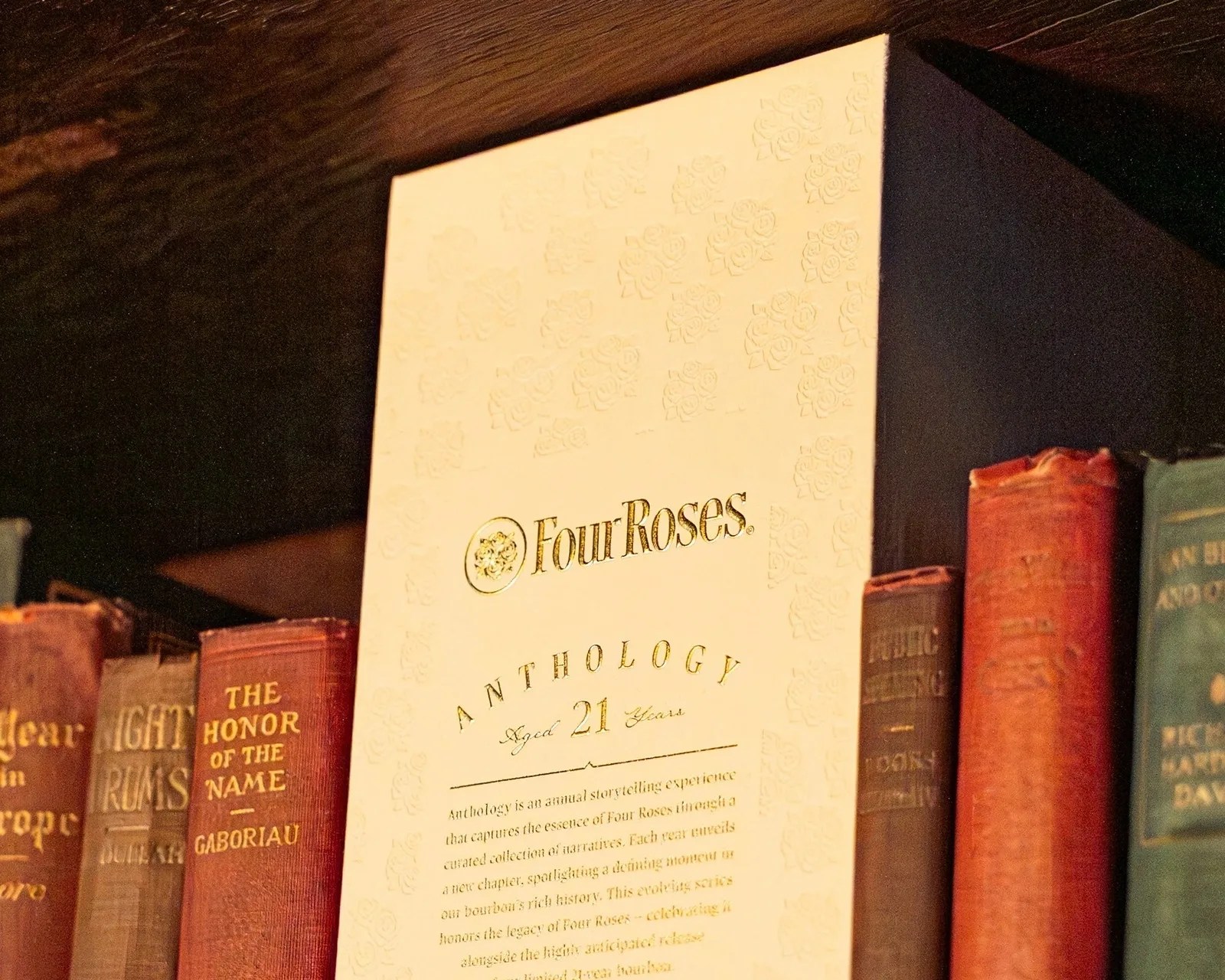 White Four Roses Anthology aged 21 years box placed among old hardcover books on a wooden shelf.