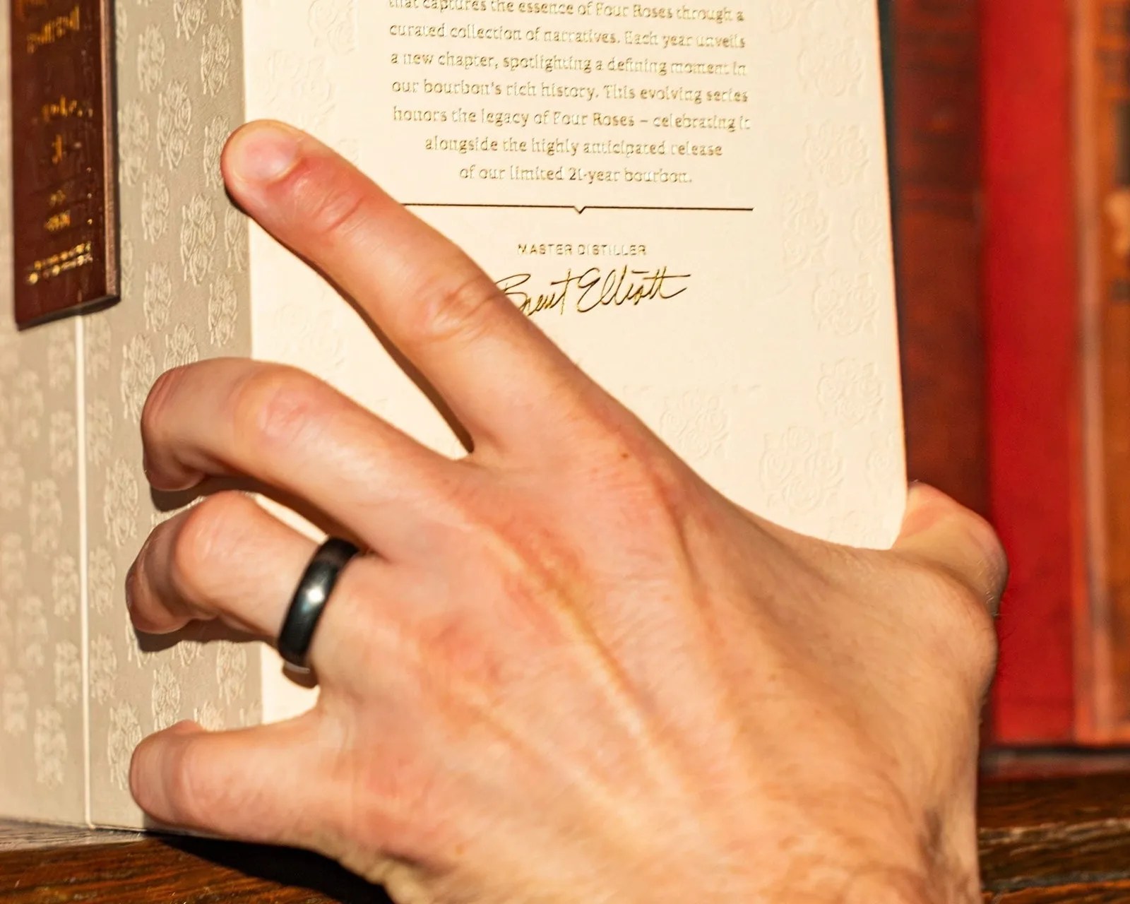Hand with a black ring holding an open book with embossed floral patterns and printed text.