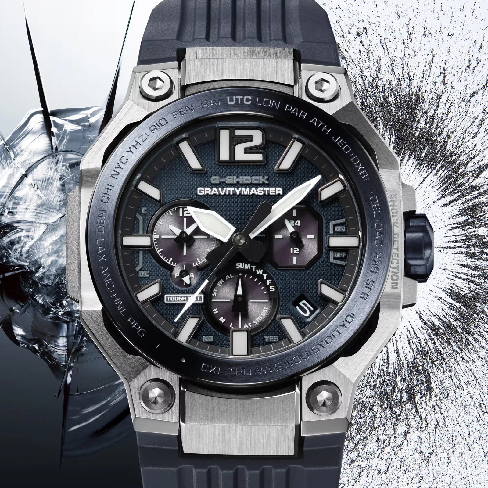 Close-up of a G-Shock Gravitymaster watch with a black dial, silver metal case, and black resin strap, shown with cracked glass background.