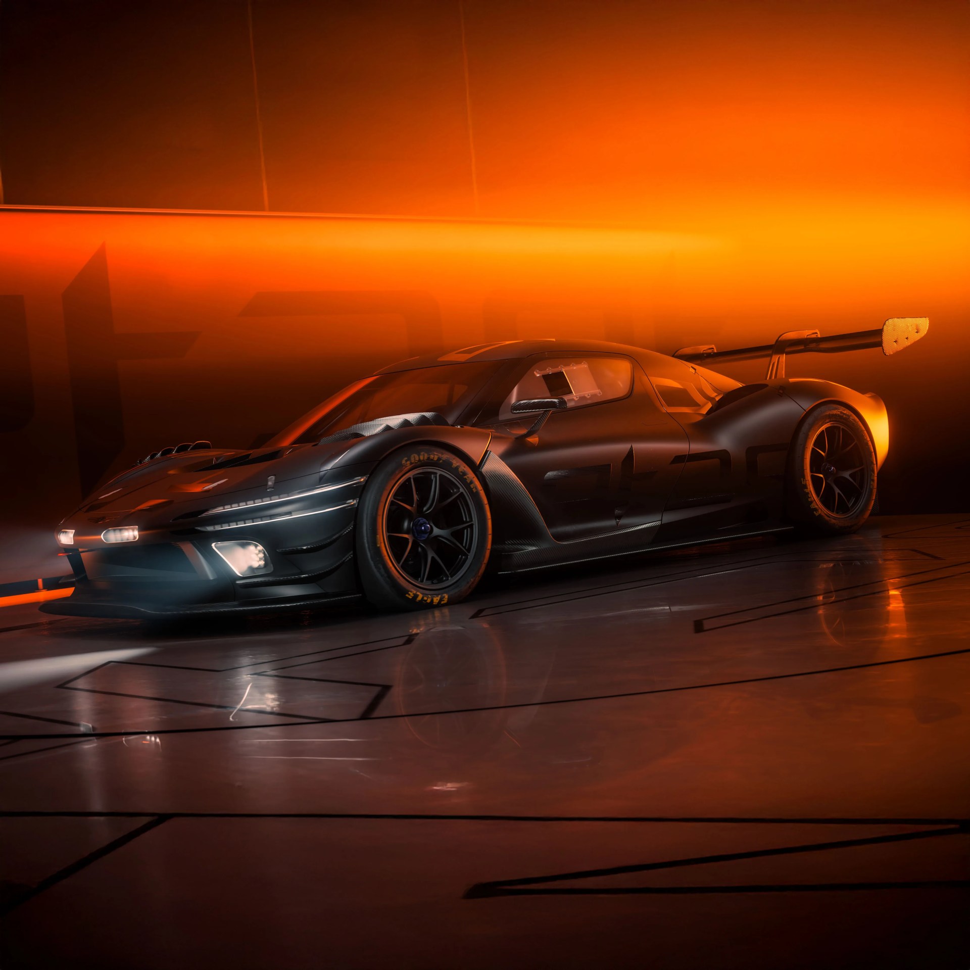 Matte black race car with aerodynamic design and large rear wing under orange lighting.