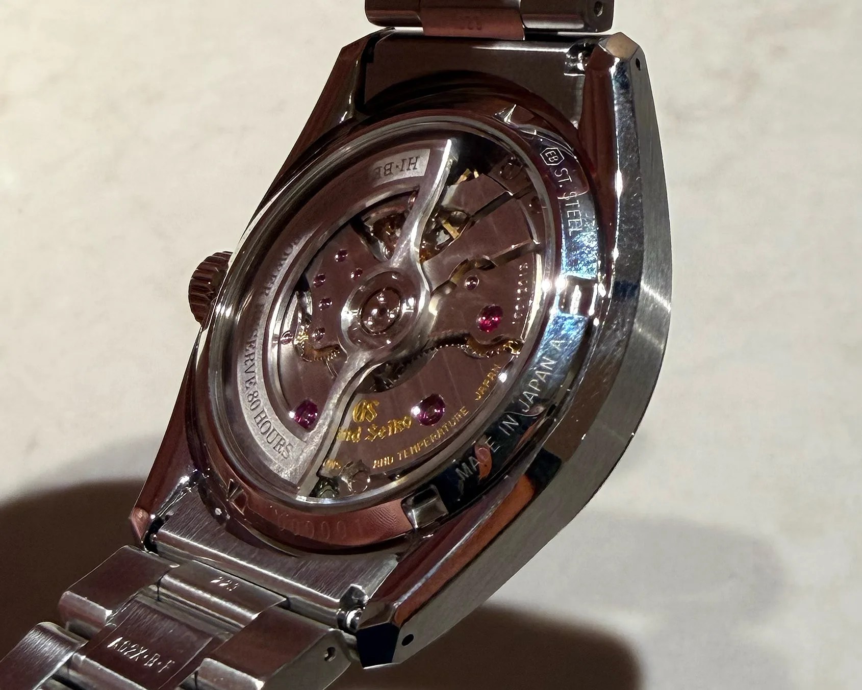 Close-up of the back of a stainless steel wristwatch showing the intricate mechanical movement with visible jewels and engravings.