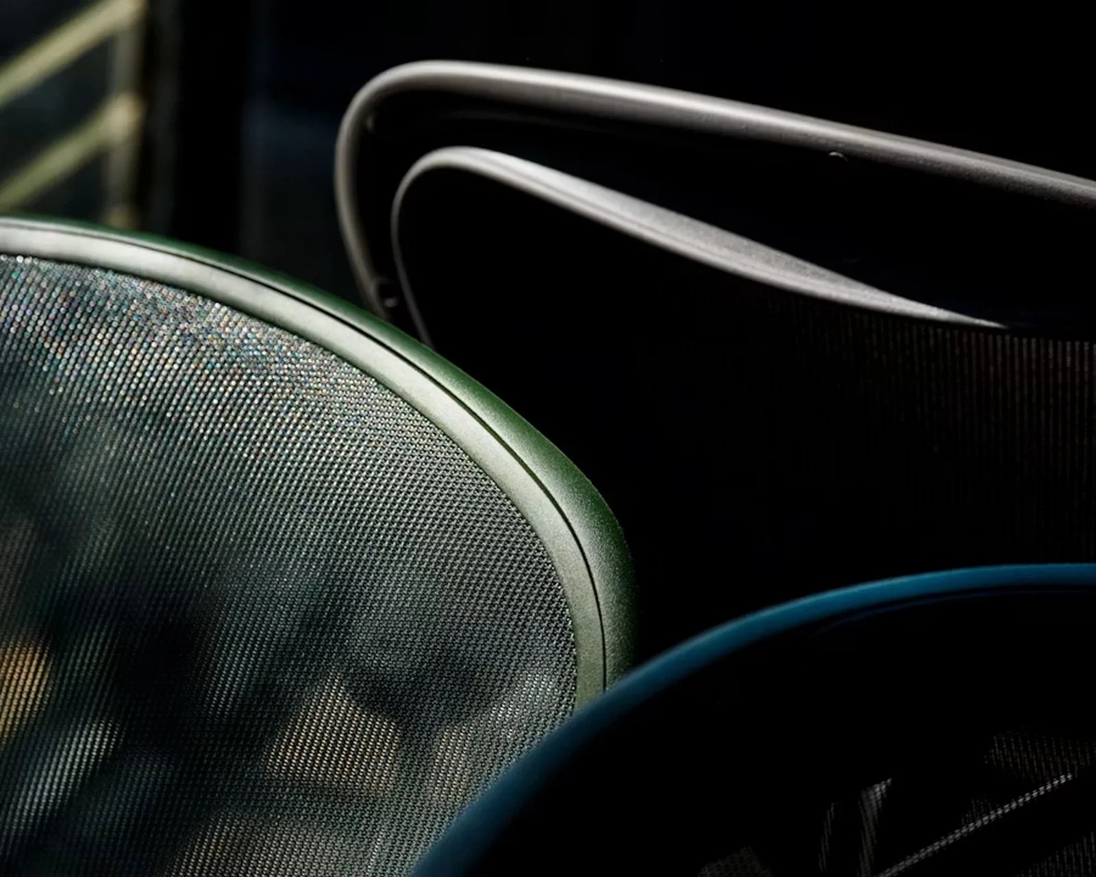 Close-up of mesh office chair backs in green, black, and blue with curved frames in low light.