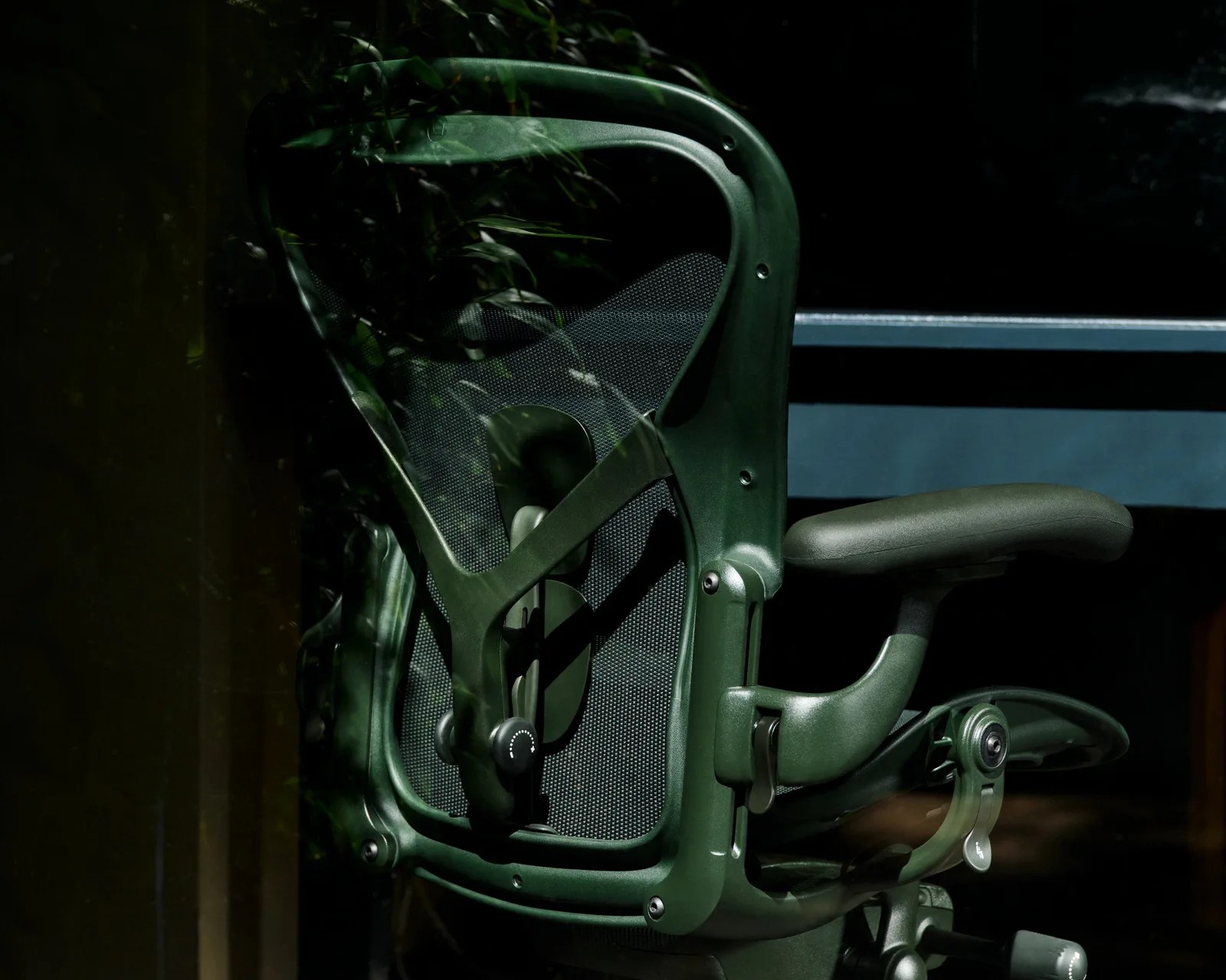Dark green ergonomic office chair with mesh back and adjustable armrest in low light.