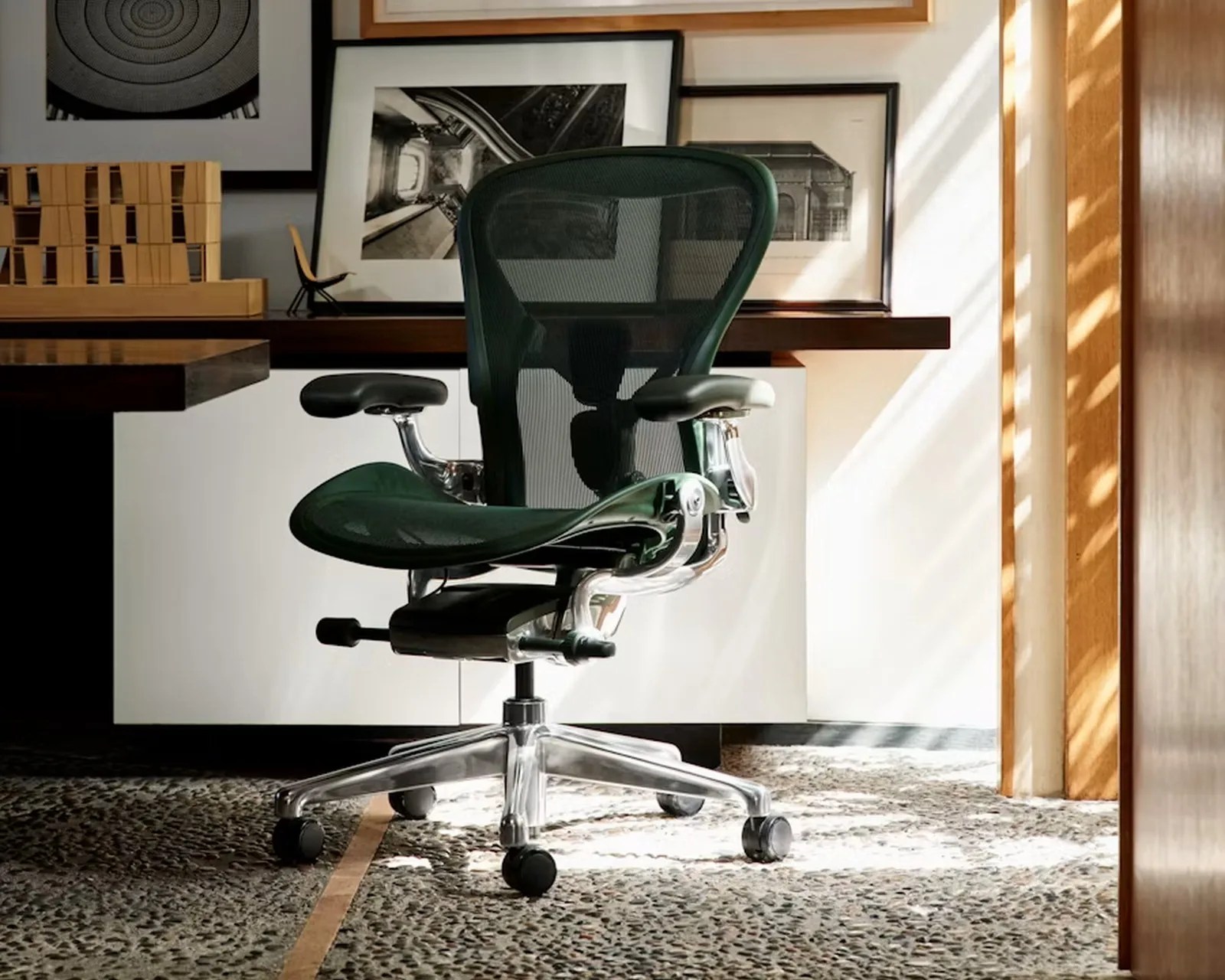 Ergonomic black mesh office chair with chrome frame and adjustable armrests on a pebble-textured floor.