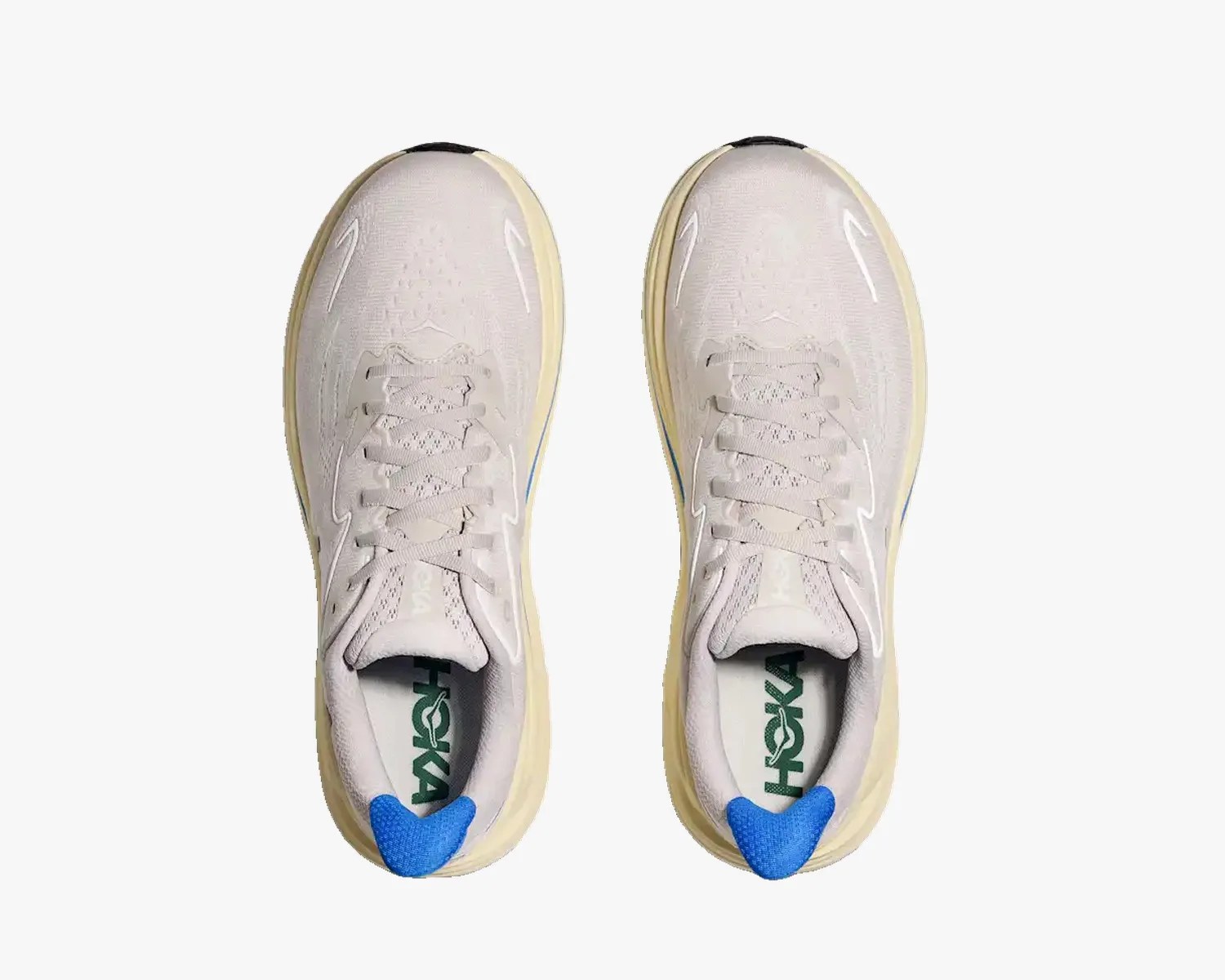 Pair of light beige Hoka running shoes with blue heel tabs and green logo on the insoles, viewed from above.
