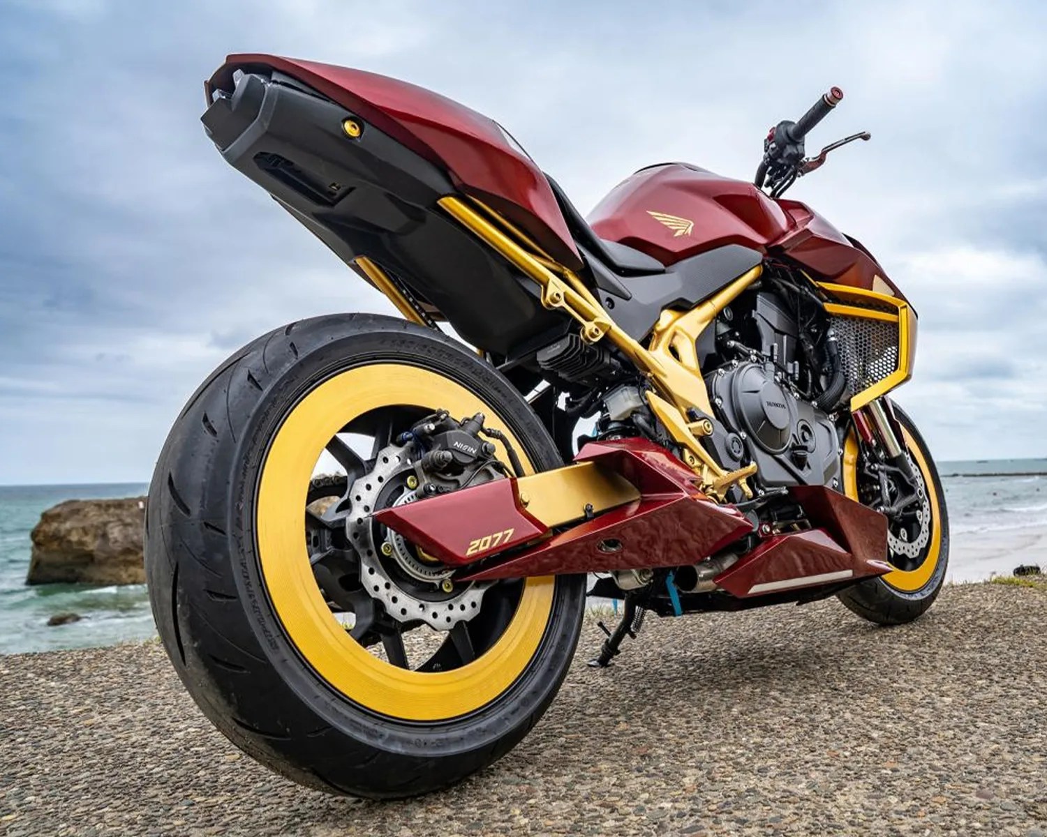 Red and gold sport motorcycle with yellow rims parked on a concrete surface near the ocean.