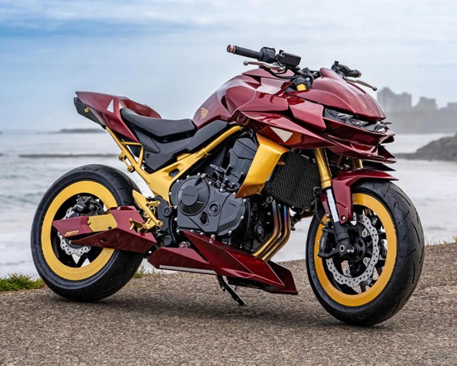 Red and gold sport motorcycle with yellow rims parked on a coastal road.