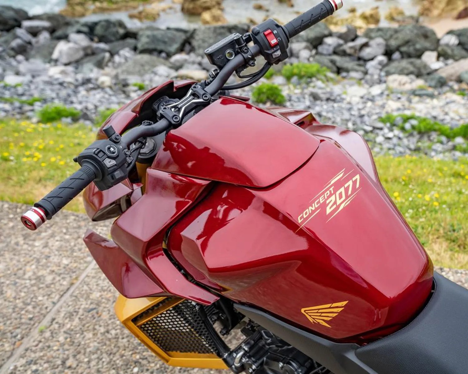 Glossy red motorcycle fuel tank with "CONCEPT 2077" text and black handlebars with red accents.