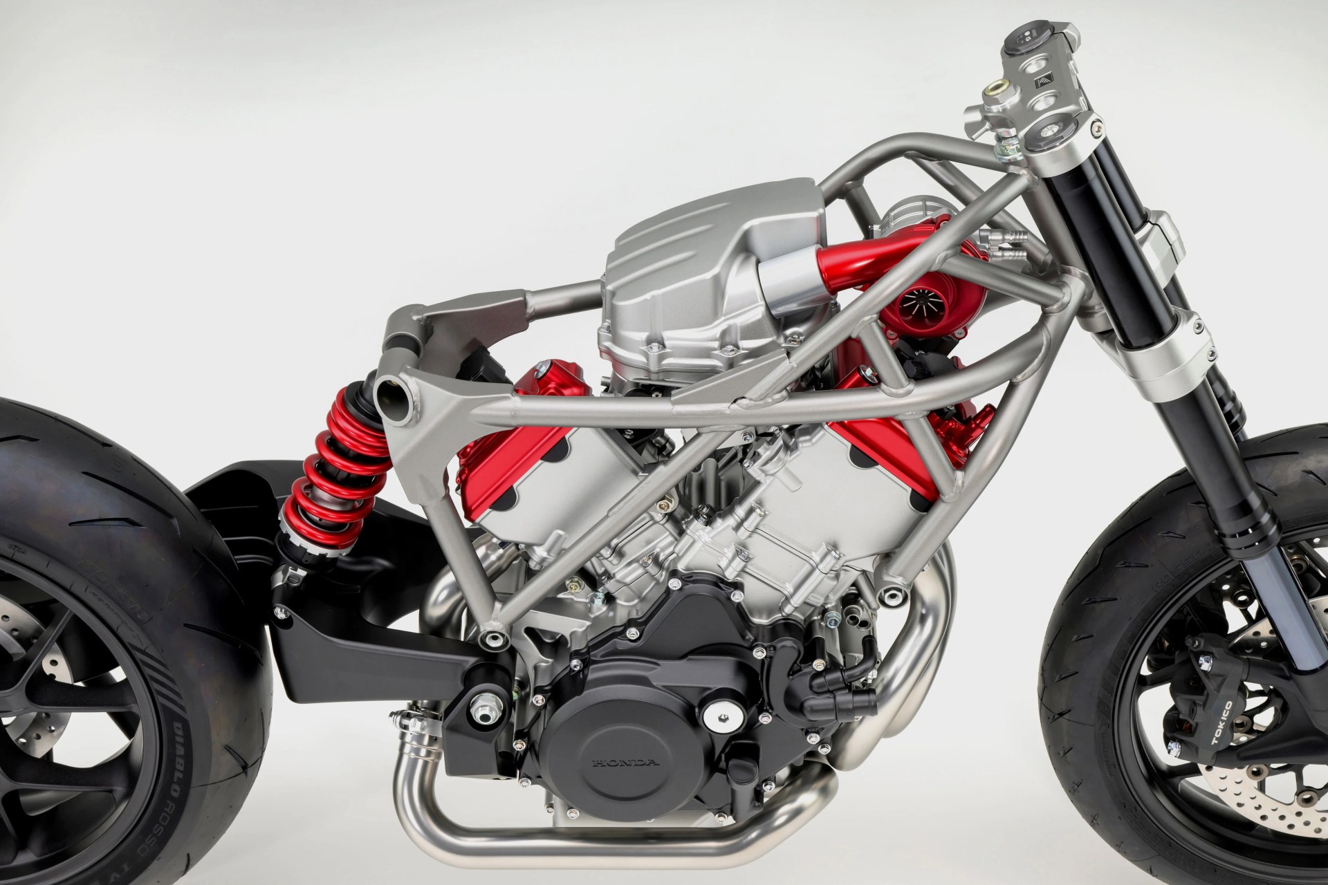Close-up of a motorcycle engine with silver frame, red components, black suspension, and black tires.