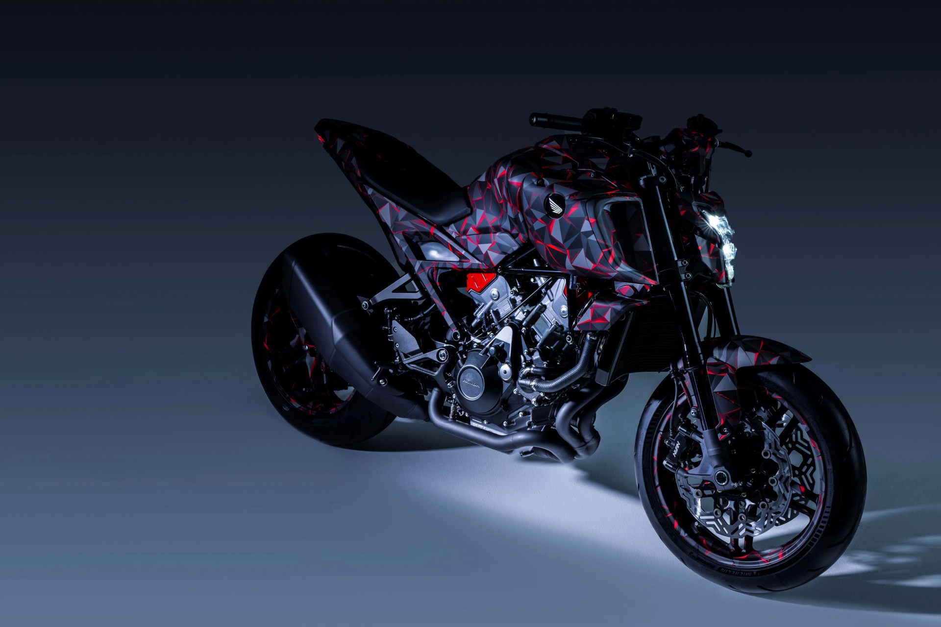 Sport motorcycle with black and red geometric patterned body and illuminated front headlight.