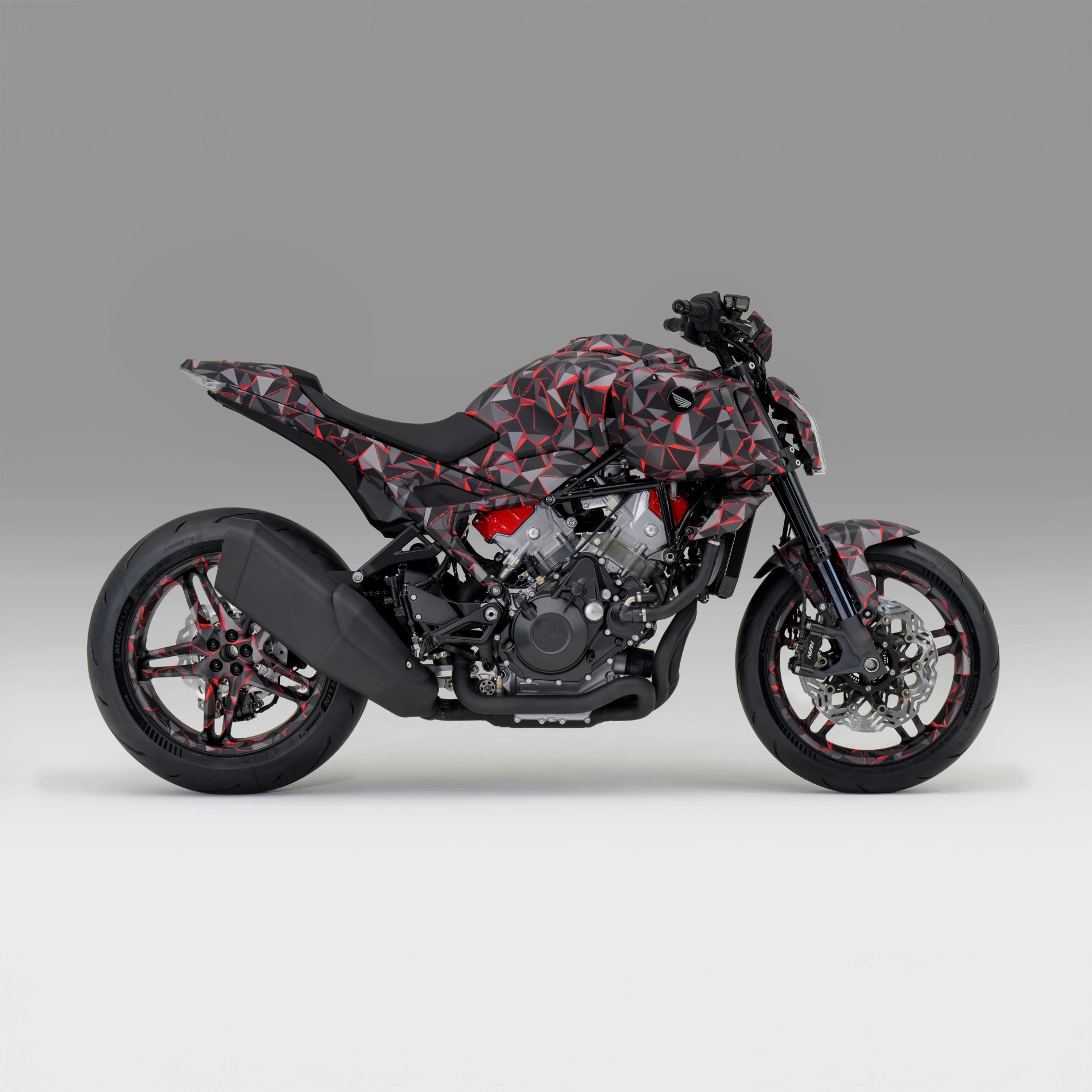 Sport motorcycle with black, red, and gray geometric camouflage pattern and exposed engine components.