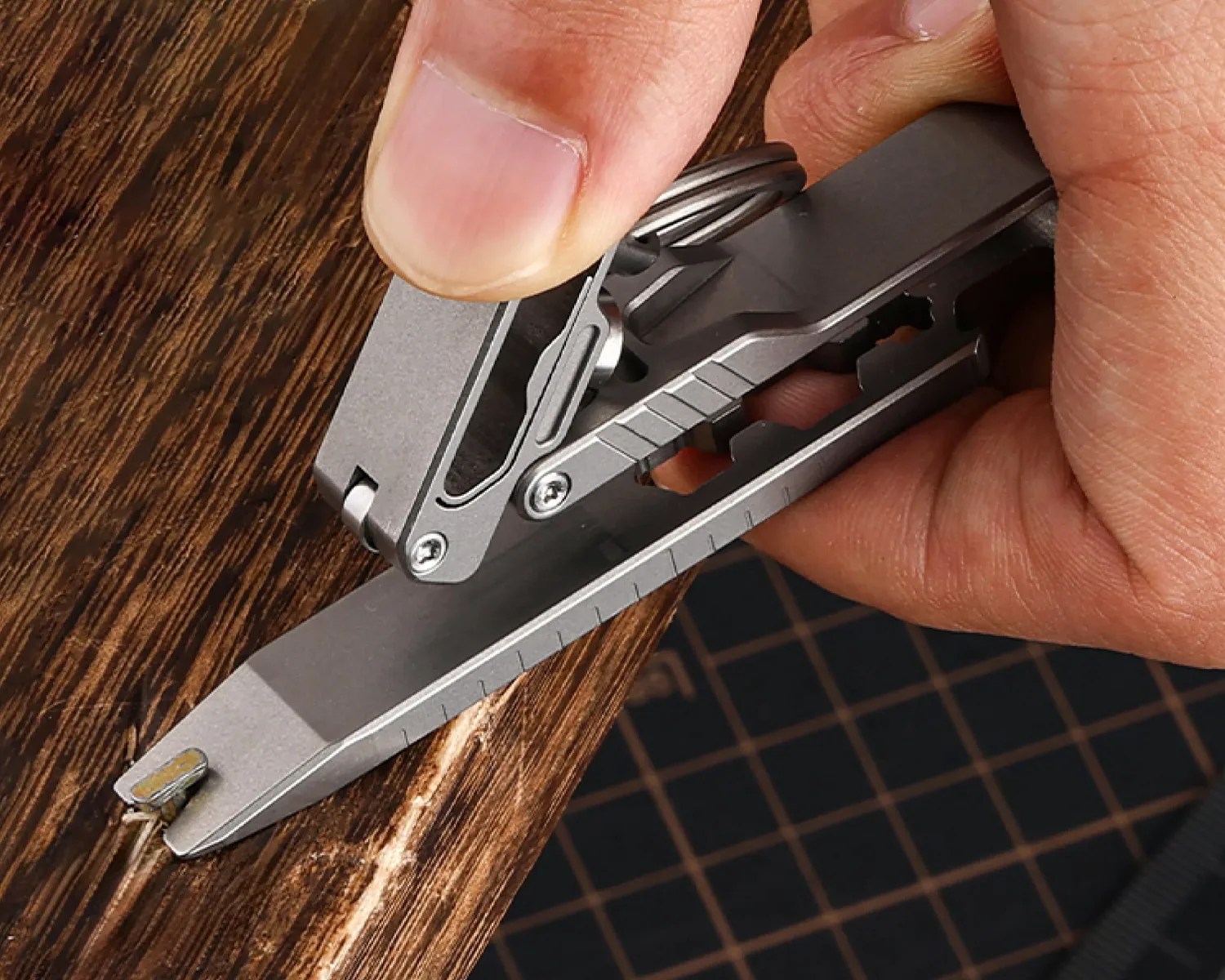 Hand holding a silver multi-tool with a flat pry bar tip lifting a nail from a wooden surface.