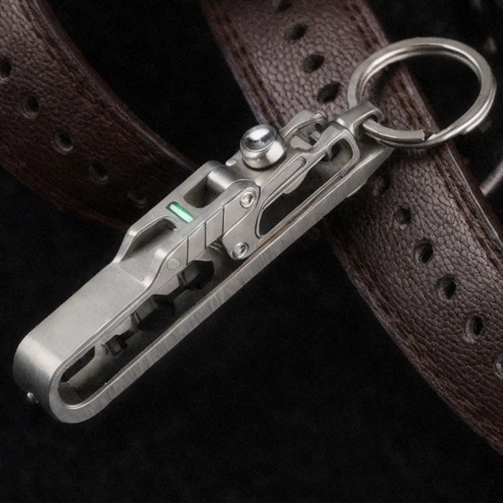 Close-up of a silver metal multi-tool with a keyring attached, resting on a brown leather strap.