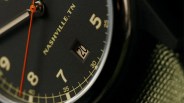 Close-up of a black watch face showing the date "20," with beige numerals and an orange second hand.